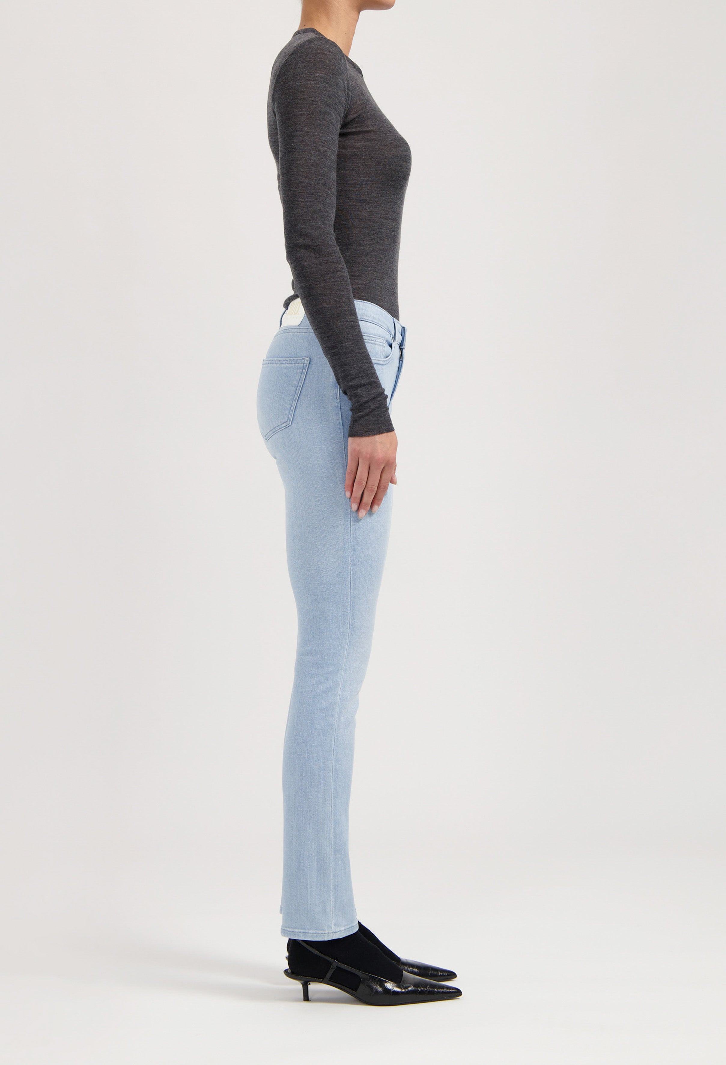 Model wearing light blue skinny jeans and a dark gray long-sleeve top with black low-heeled shoes.