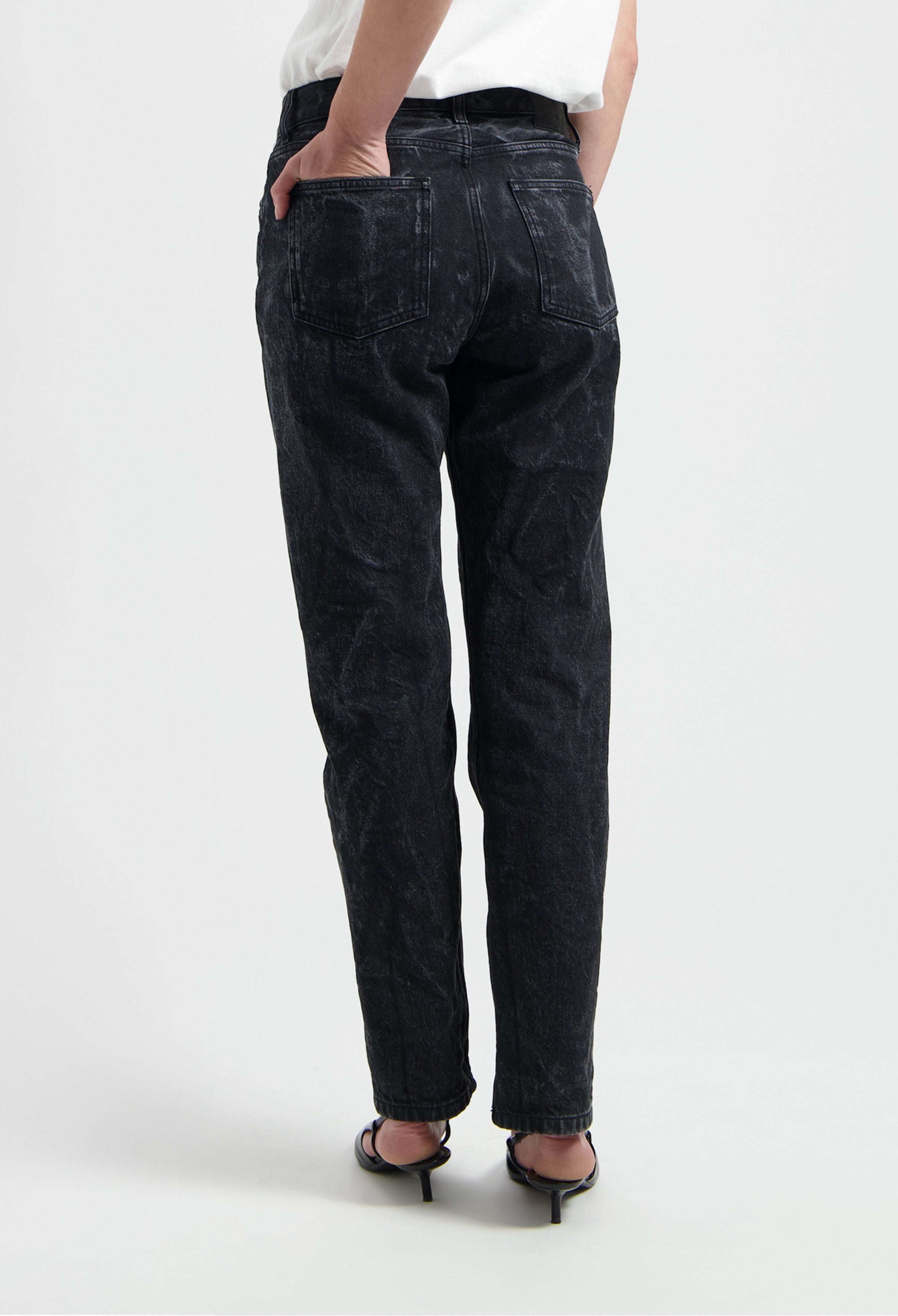 Black denim jeans with a relaxed fit and classic pockets, styled with a simple white top and black heeled sandals.