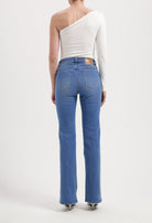 Model wearing blue high-waisted denim jeans with straight legs, paired with a one-shoulder white long-sleeve top.