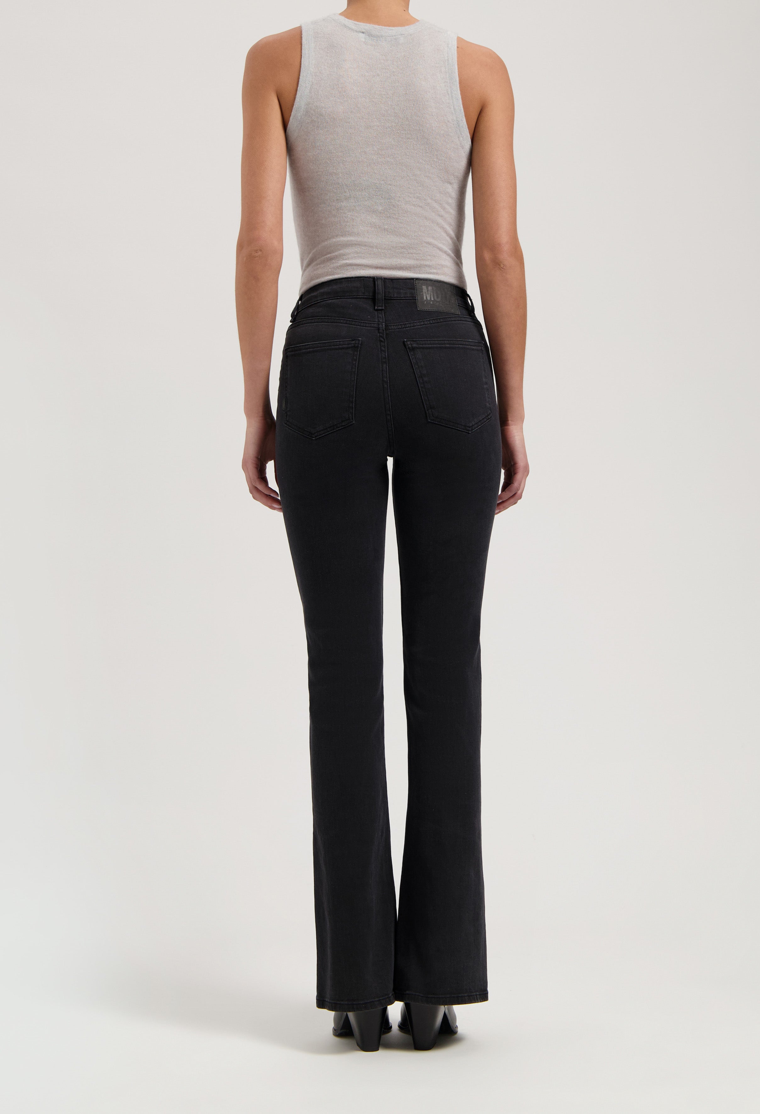 Back view of black high-waisted denim jeans worn with a sleeveless gray top, showcasing flared legs and sleek silhouette.