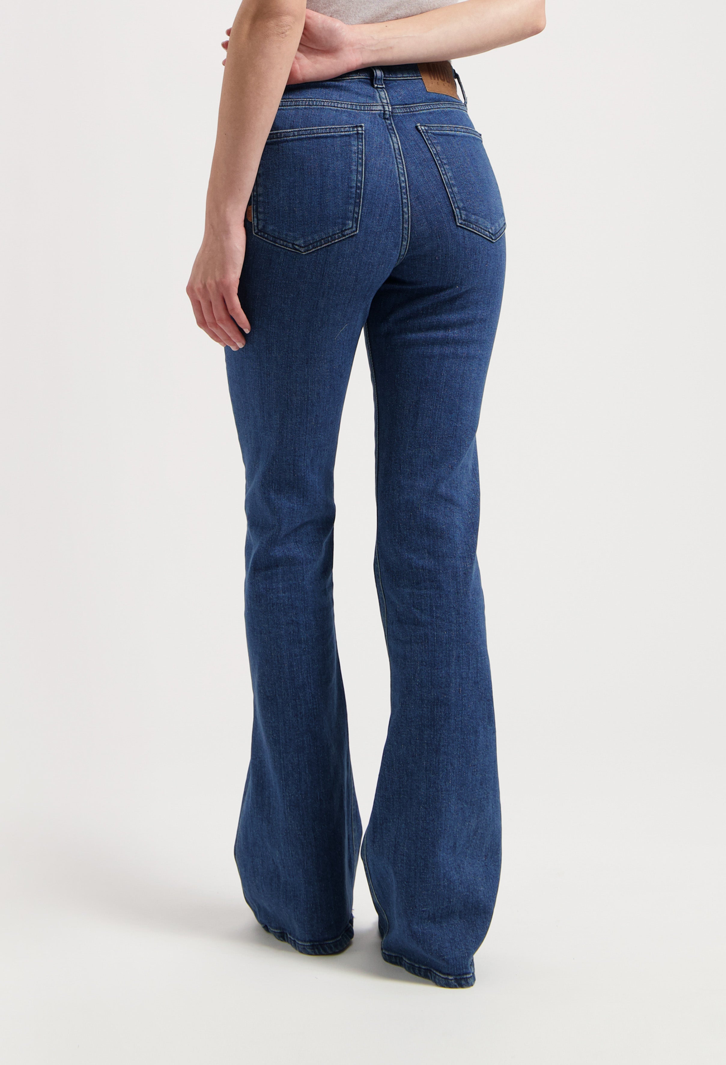 Woman wearing bootcut blue jeans made from eco-friendly denim, showcasing rear view details with pockets and seam stitching.