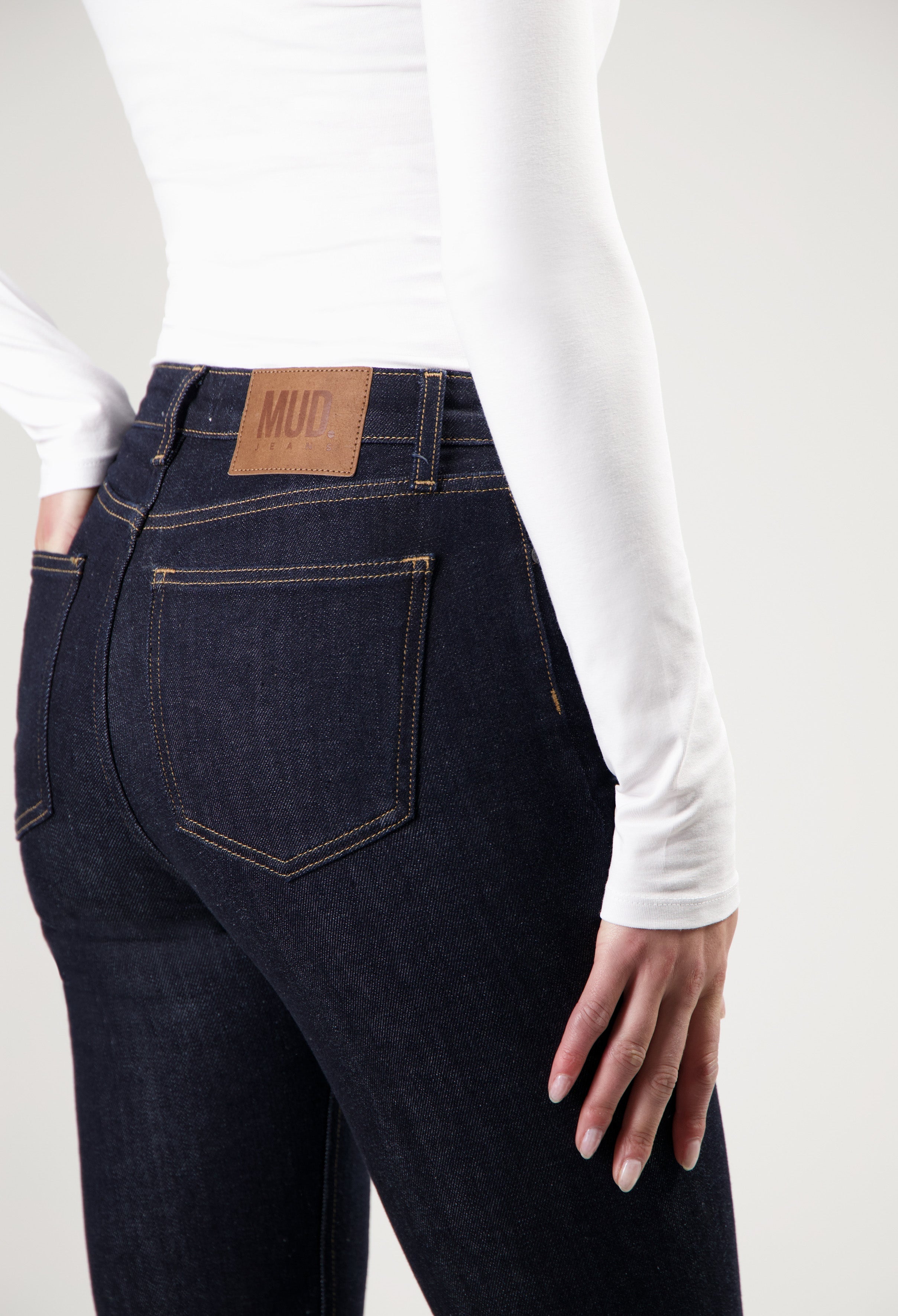 Dark blue, slim-fit MUD Jeans from organic cotton, showcased from the back with white long-sleeve top detail.
