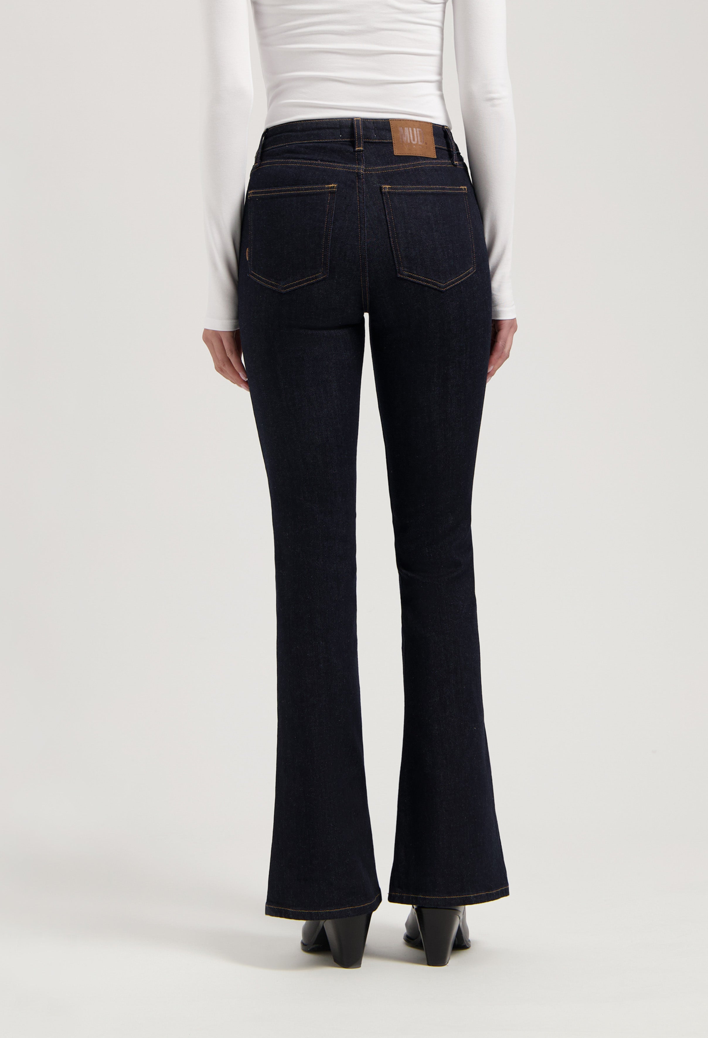 Flared dark blue jeans in organic cotton, worn with a fitted white long-sleeve top, showcasing a rear view design.