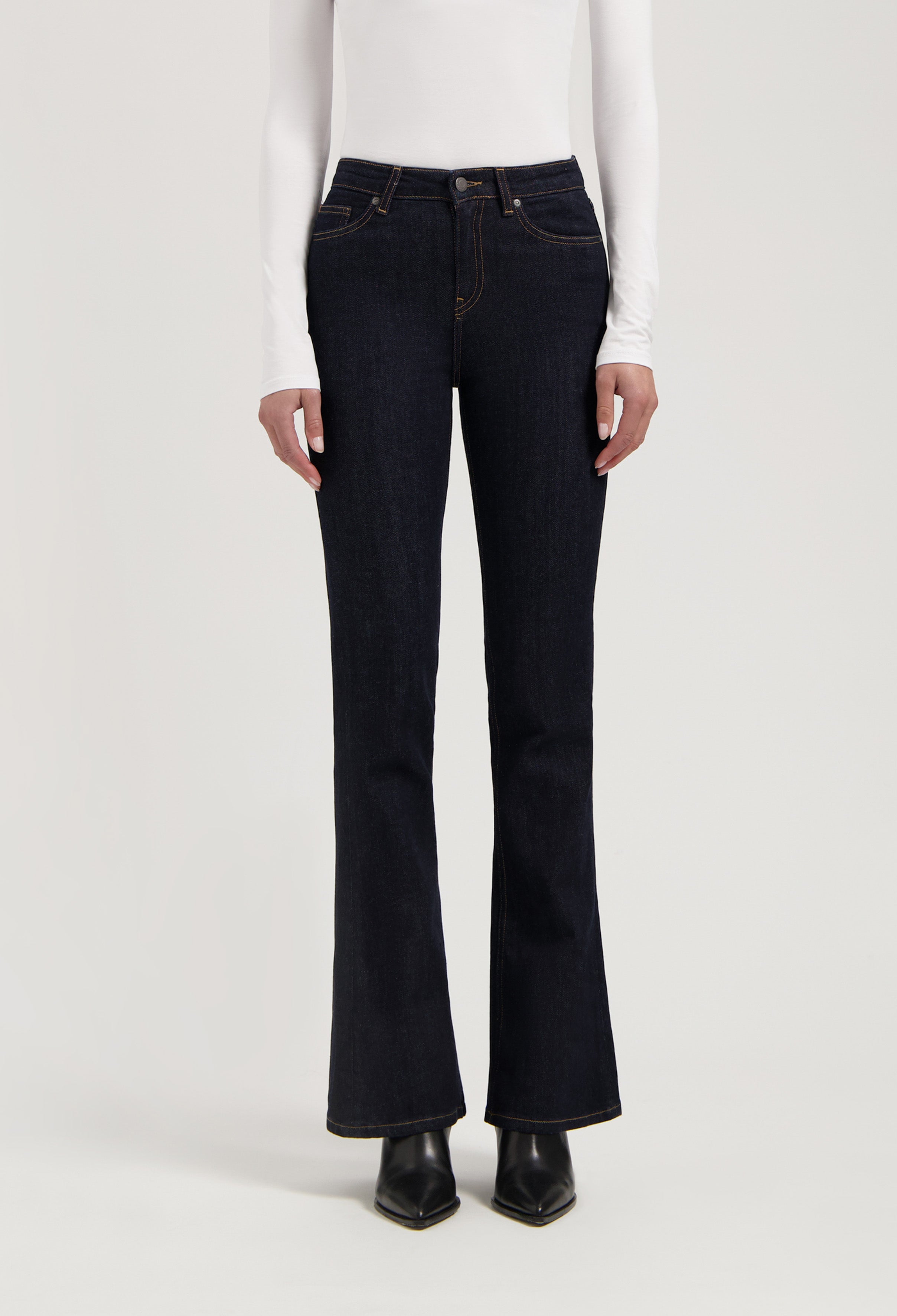 Dark indigo flared denim jeans paired with a white long-sleeve fitted top, showcasing classic contrast stitching.