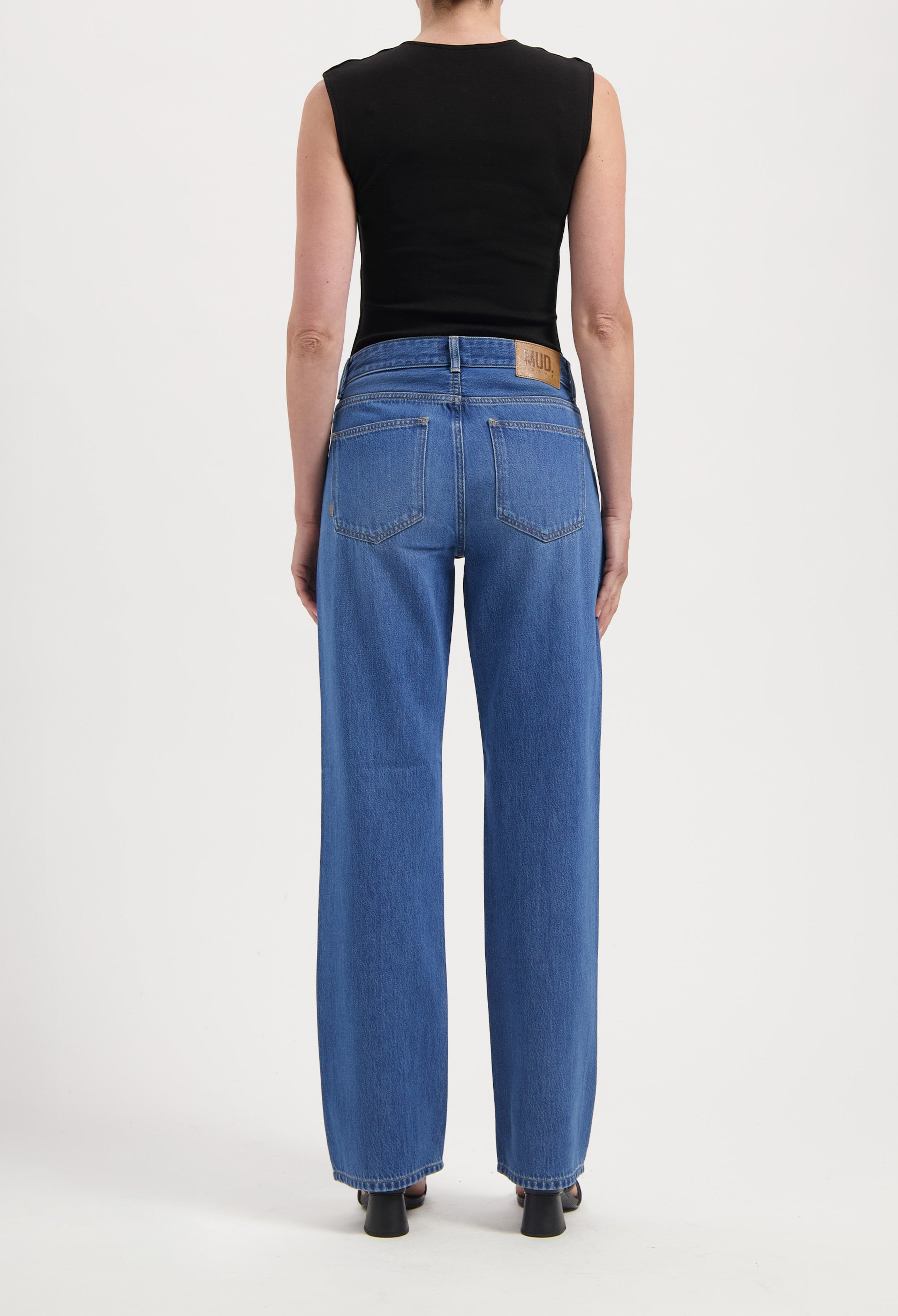 Back view of person wearing classic MUD Jeans in medium blue, wide-leg style, paired with a sleeveless black top.