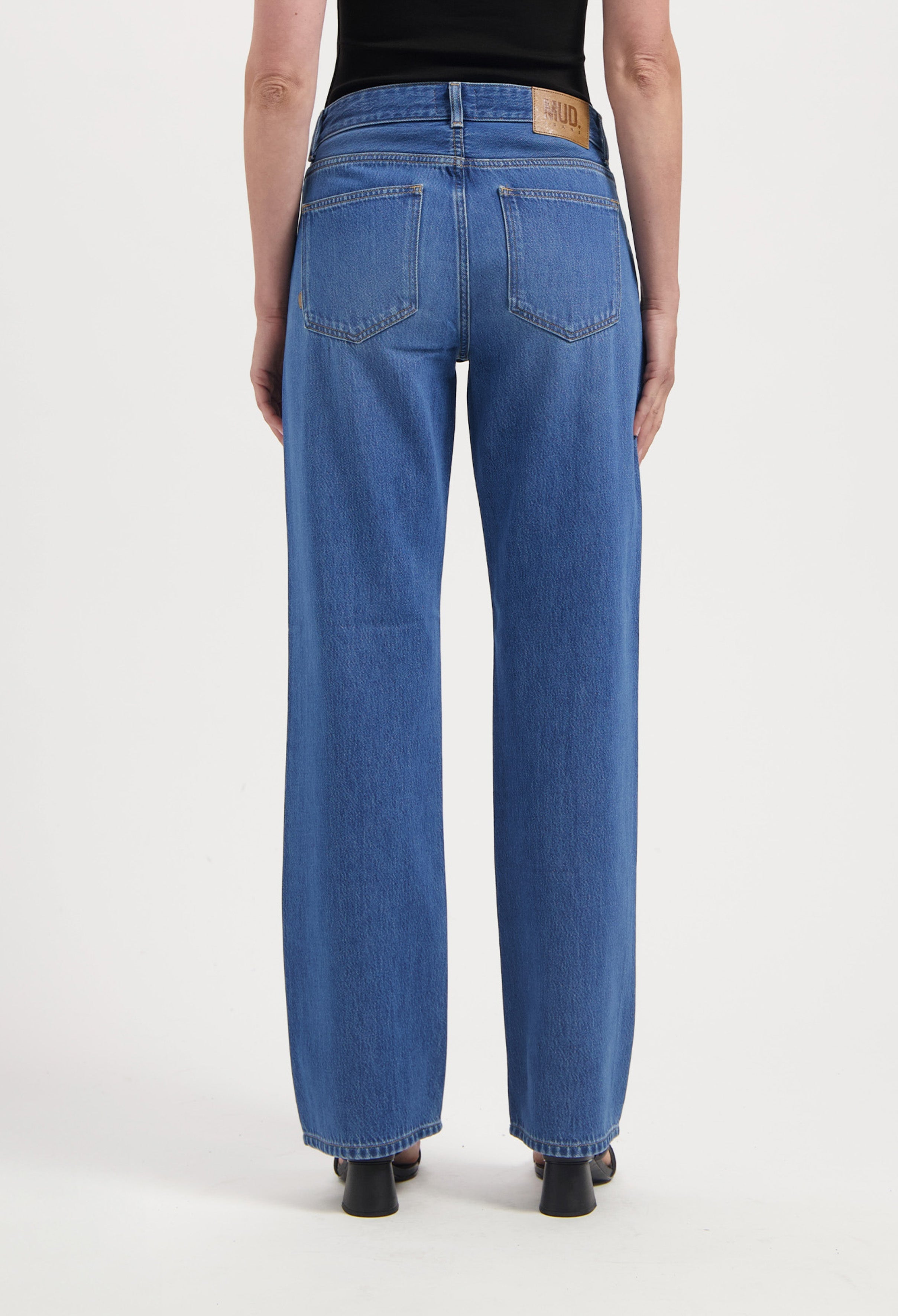 Back view of sustainable wide-leg jeans in indigo, styled with a simple black sleeveless top and black heeled shoes.