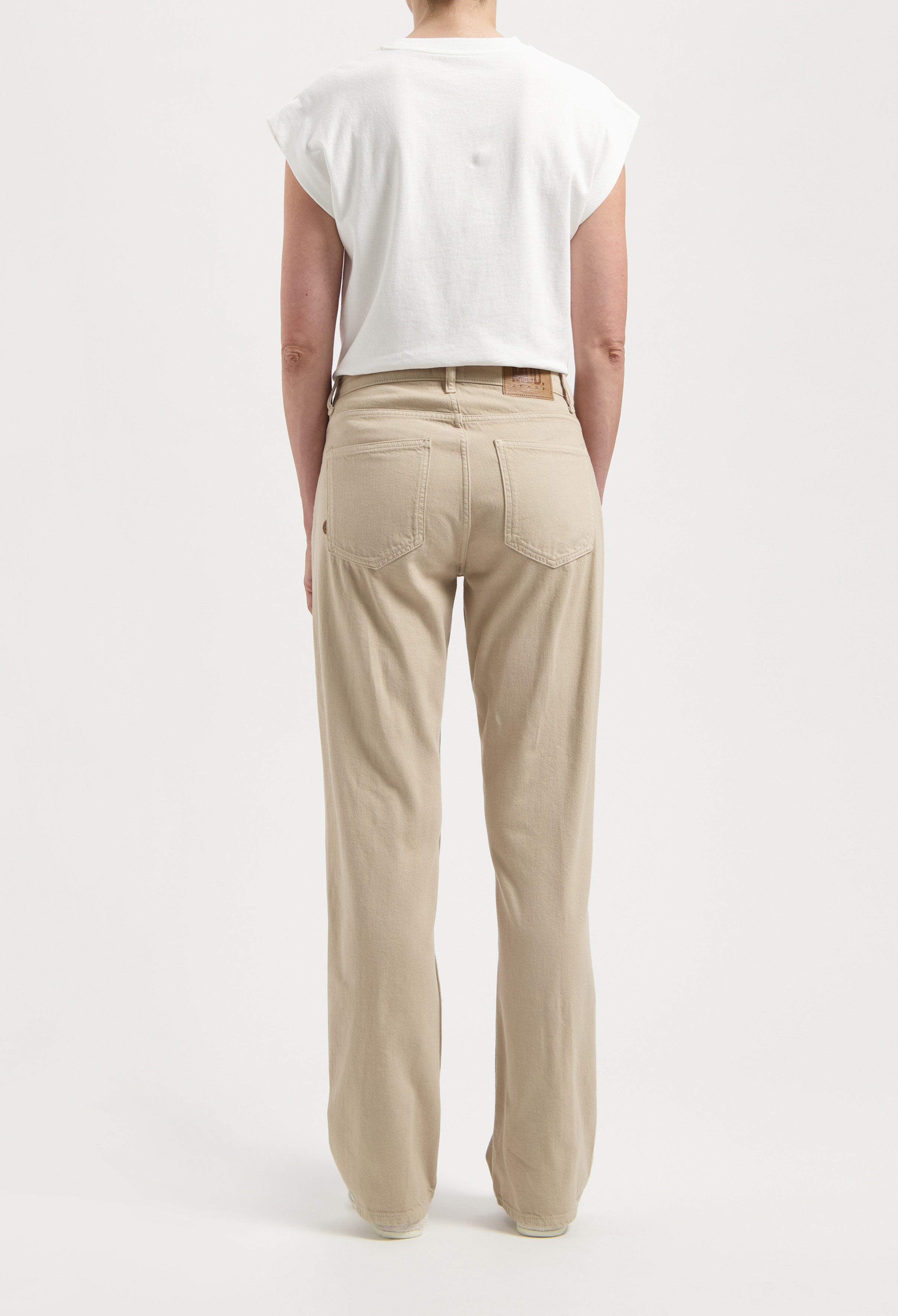 Person wearing beige high-waist denim jeans with relaxed fit, paired with a casual white sleeveless top against a plain background.