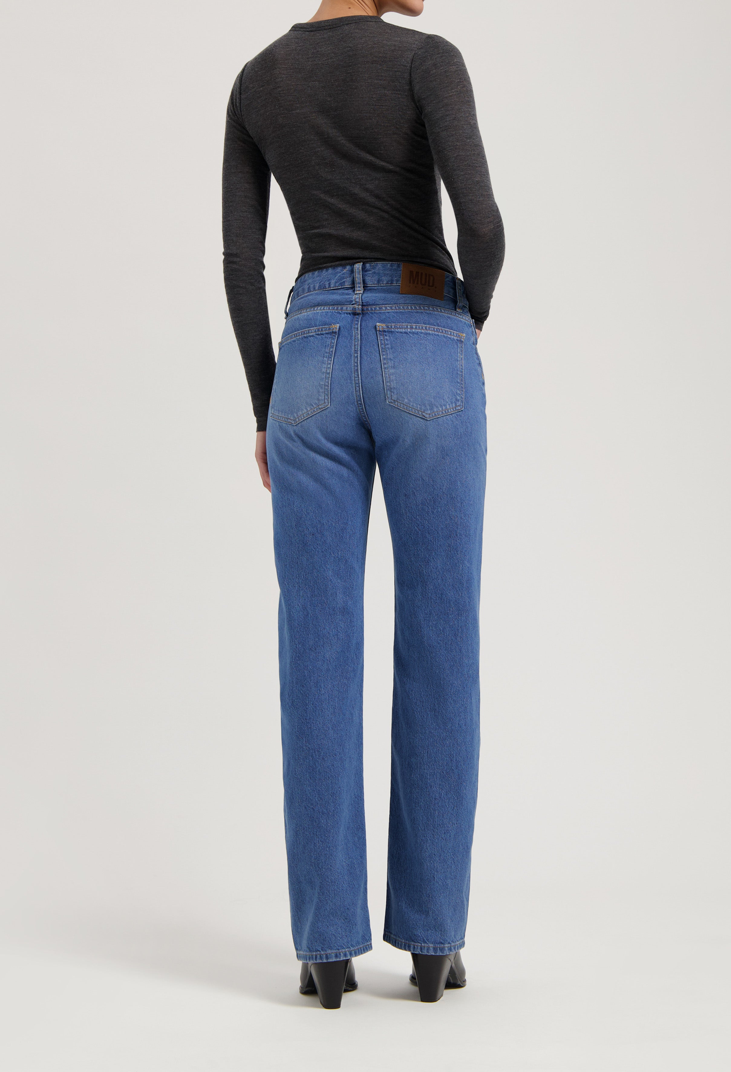 Person wearing high-waisted MUD Jeans made from organic cotton, medium blue wash, with a dark gray long-sleeve top.