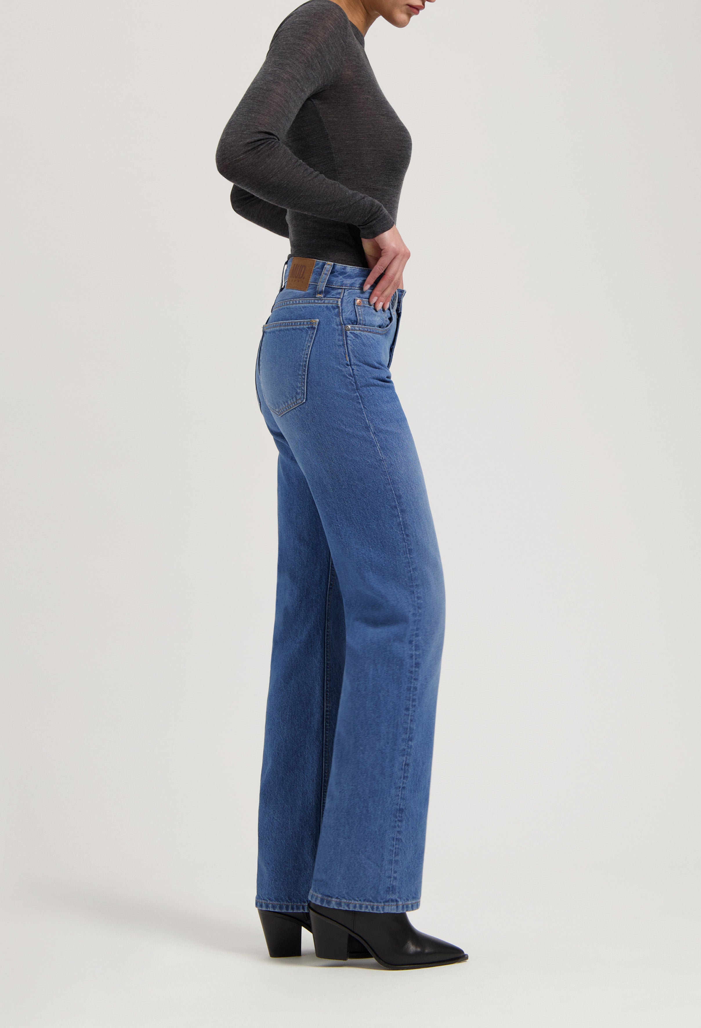 Model wearing high-waisted, wide-leg MUD Jeans in light blue denim with classic details, paired with a fitted dark gray top.
