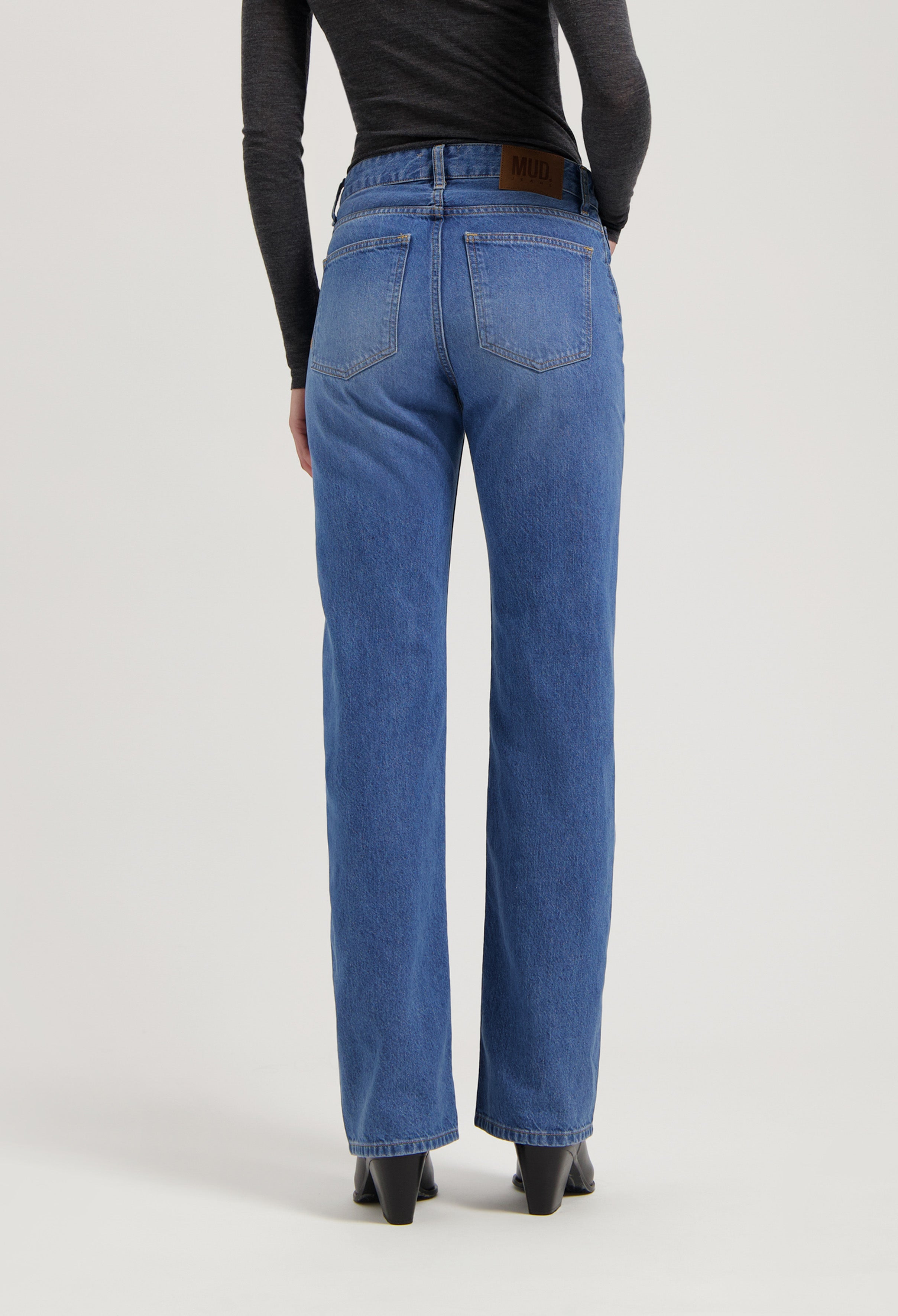 Rear view of classic straight-leg blue MUD Jeans made from organic cotton, paired with a fitted dark gray long-sleeve top.