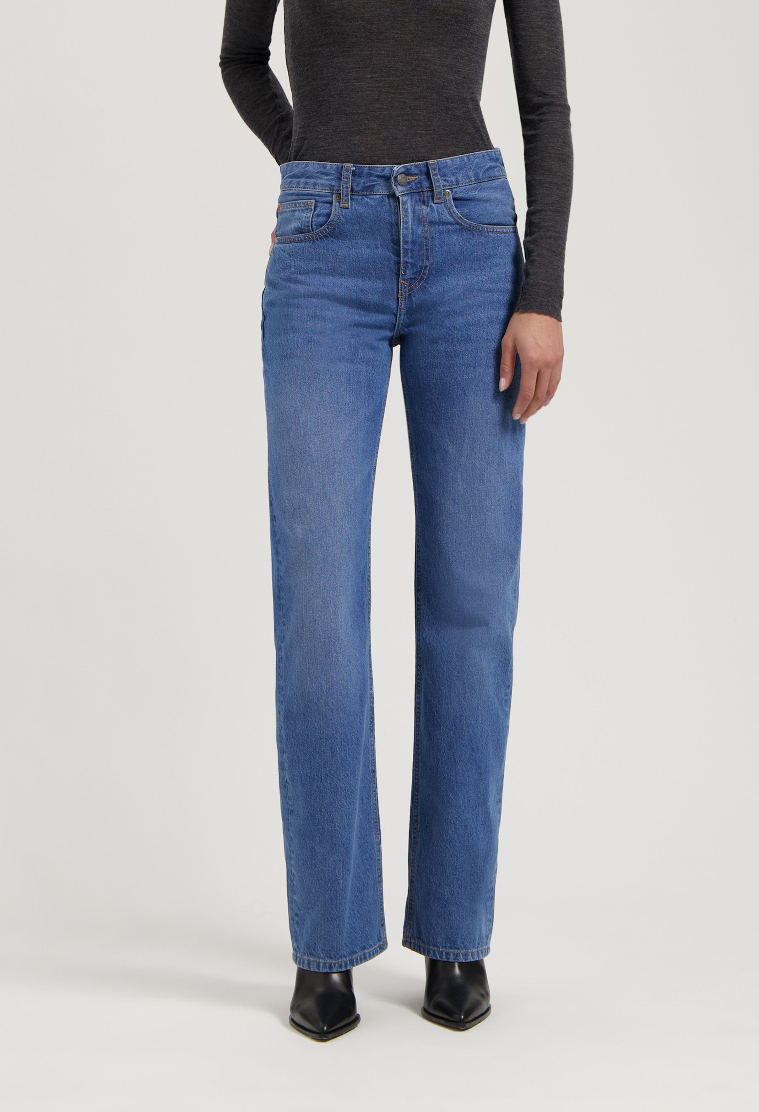 Model wearing mid-rise blue denim jeans with a straight-leg fit, paired with a dark gray long-sleeve top and black boots.