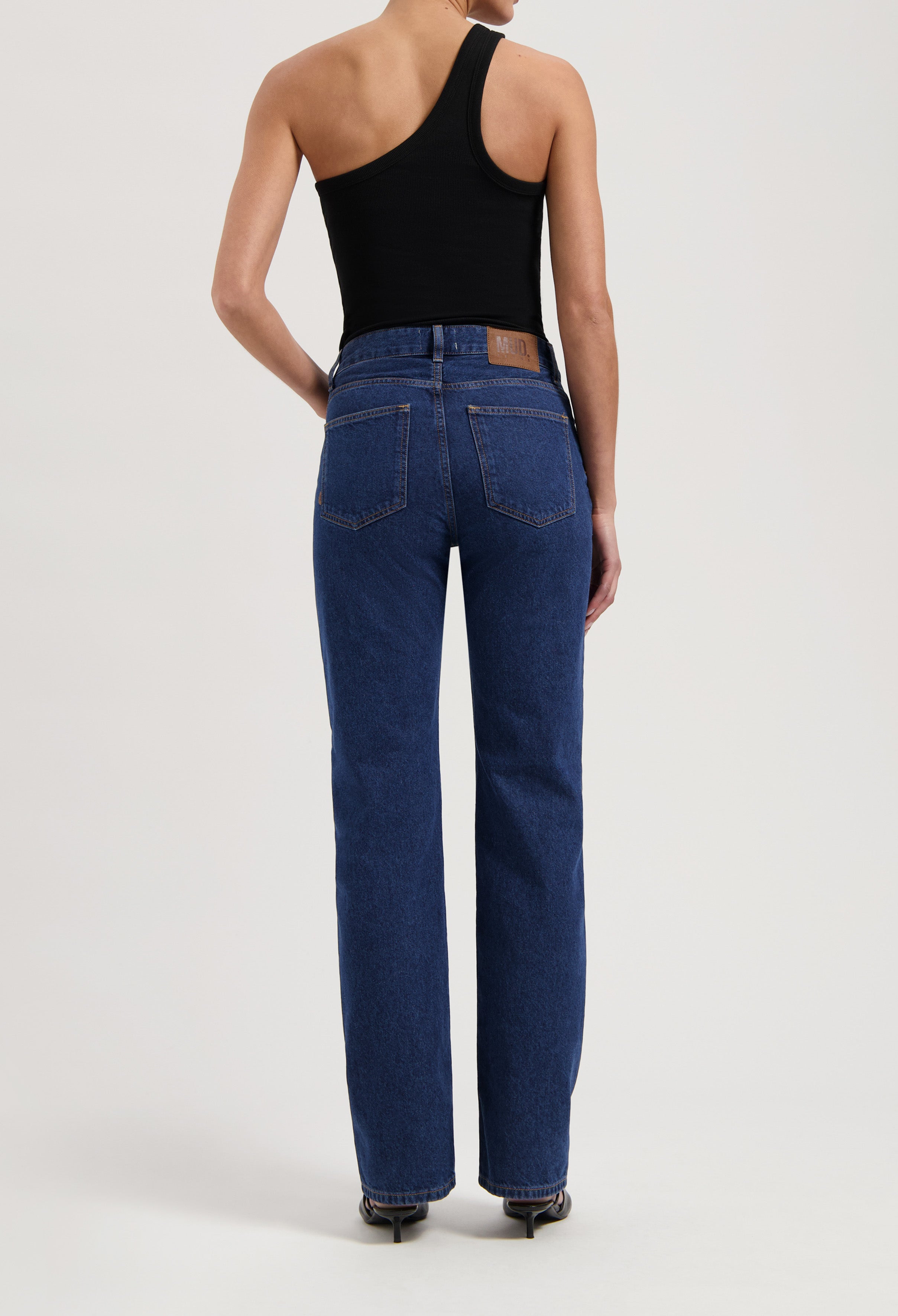 Back view of a woman wearing MUD Jeans made from organic cotton in a dark blue wash with a one-shoulder black top.