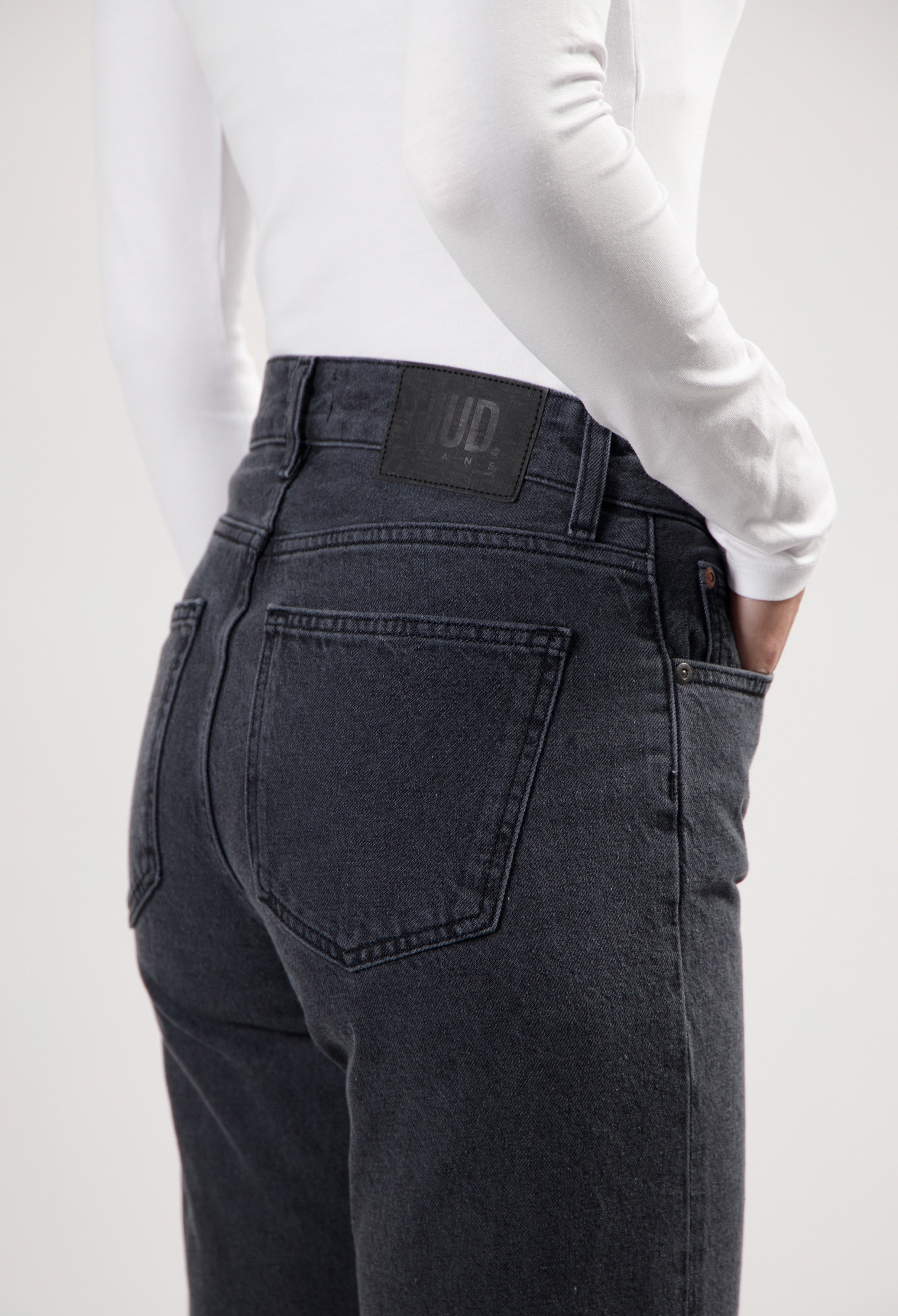 Dark blue, high-waisted denim jeans by MUD Jeans, featuring a back logo patch, paired with a white long-sleeve top.