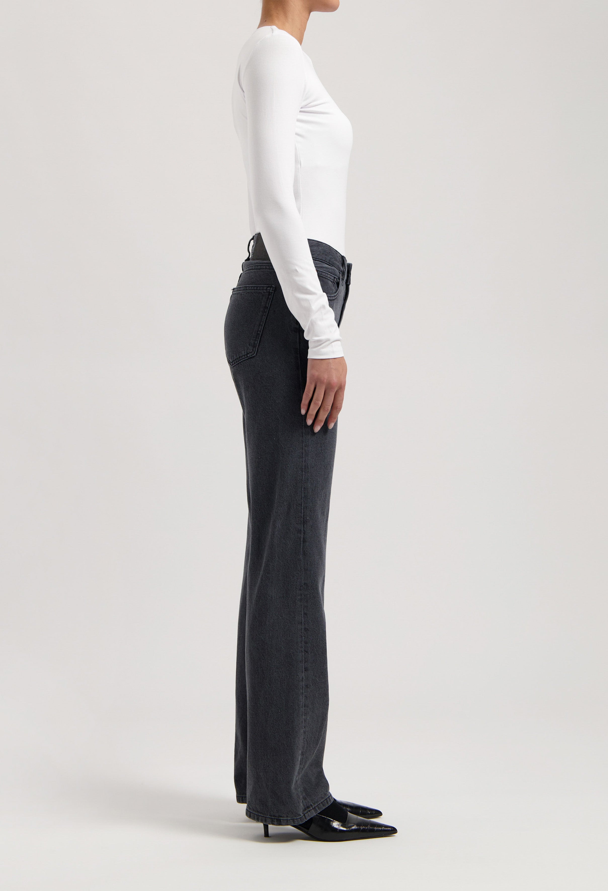 Woman wearing classic fit high-waisted charcoal jeans with a white long-sleeve top and black pointed shoes.