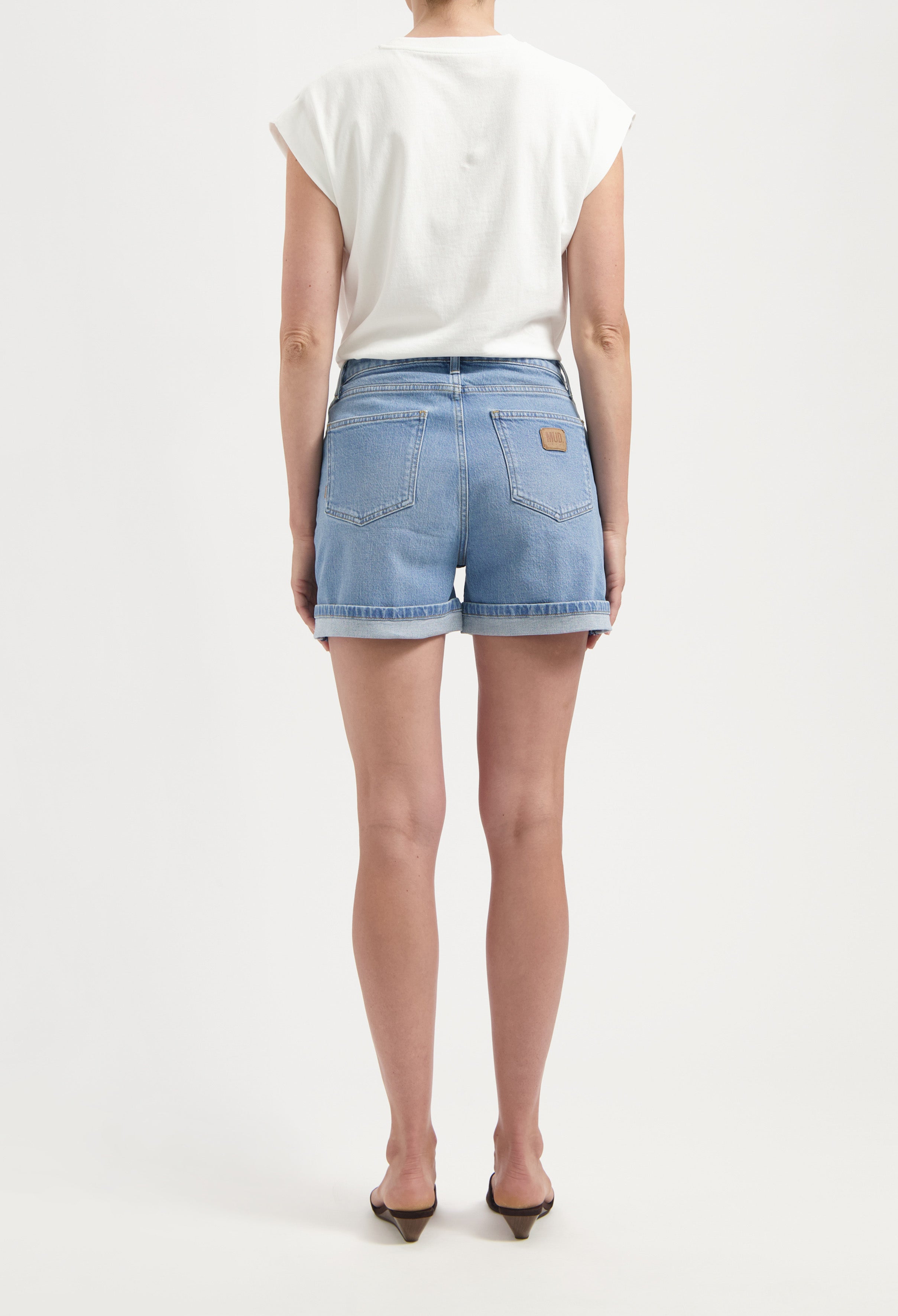 Back view of light blue denim shorts with rolled hems paired with a sleeveless white top, showcasing casual summer fashion.