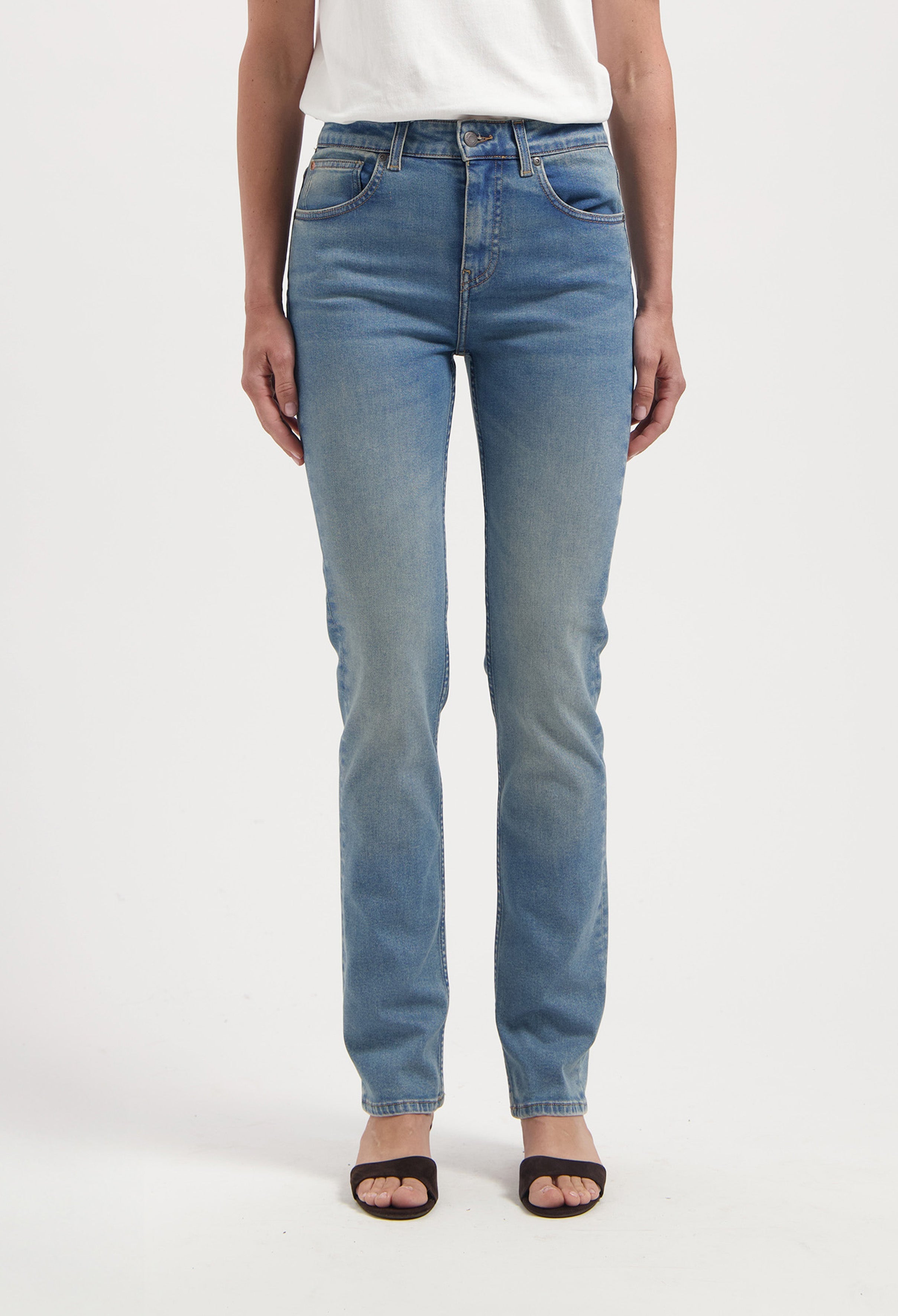 Woman wearing light blue straight-leg jeans made from organic denim, paired with a simple white tee and black sandals.