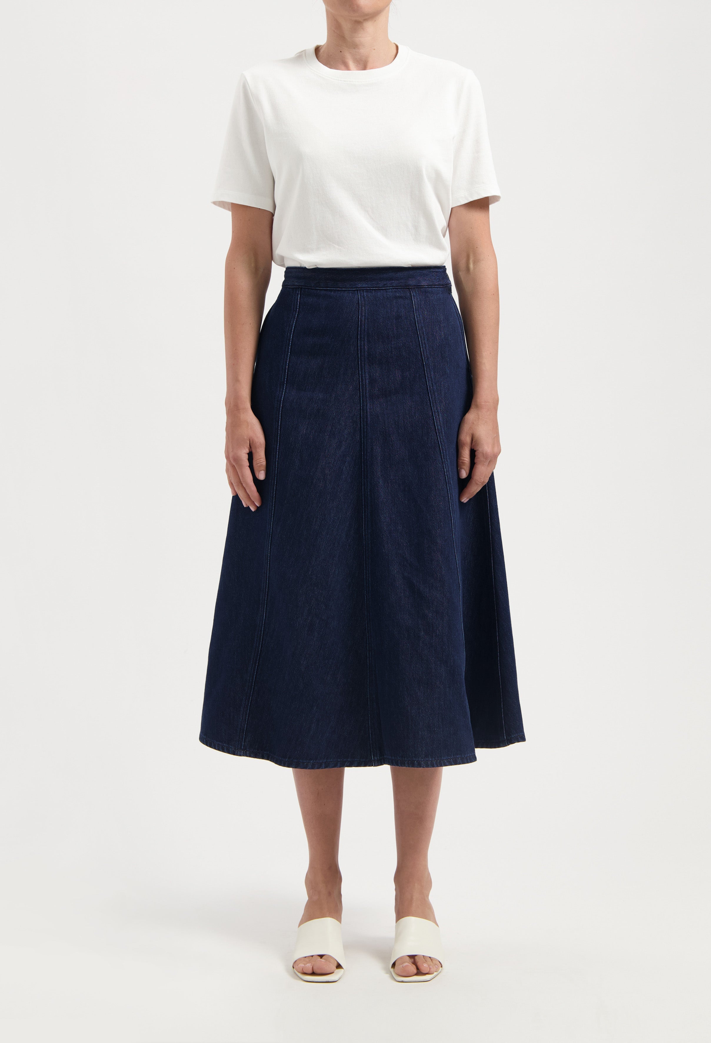 Woman wearing a white short-sleeve tee with a high-waisted navy blue denim midi skirt and white open-toe sandals.