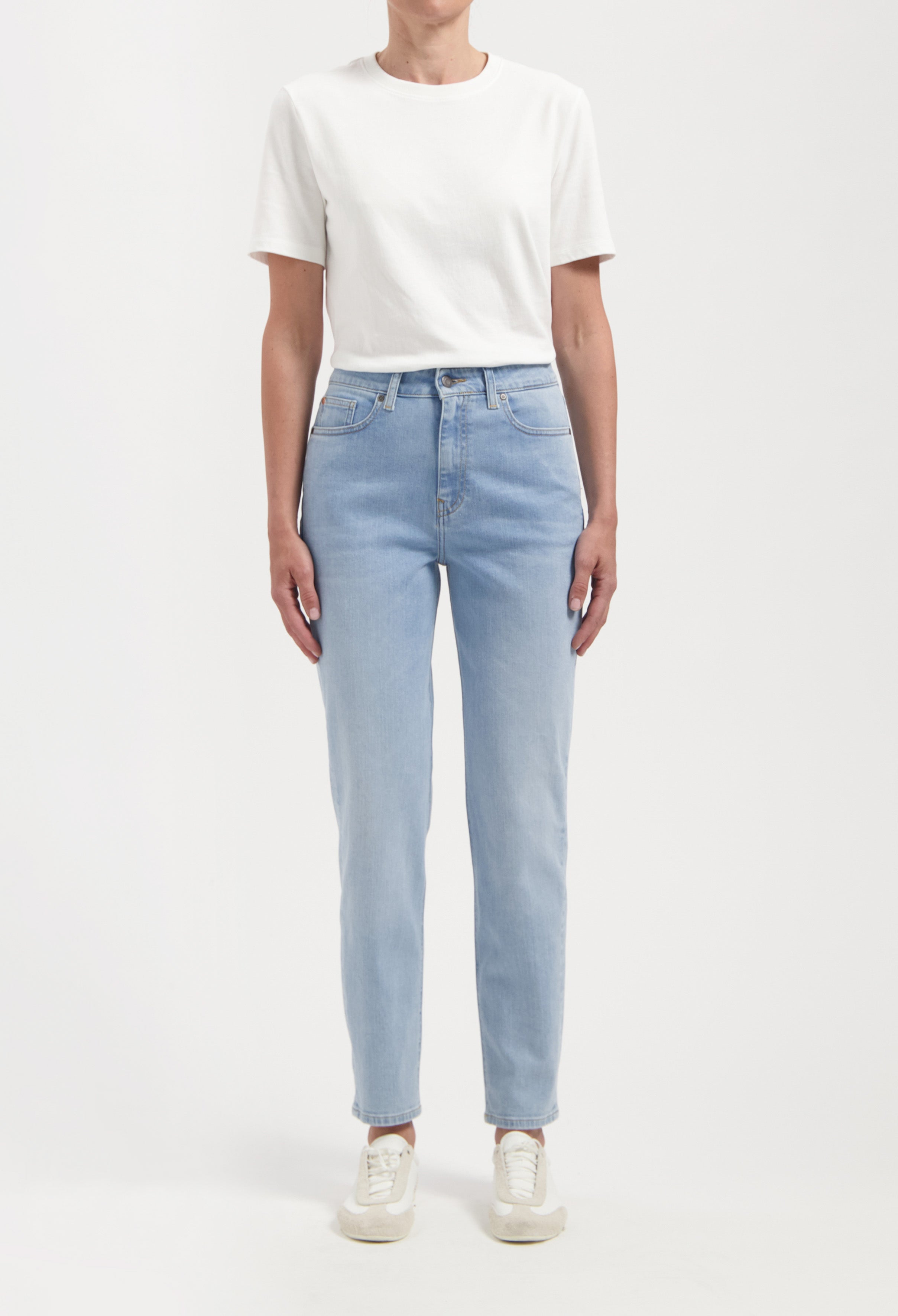 Casual outfit with light blue, high-waisted jeans and a plain white t-shirt, paired with white sneakers against a plain background.