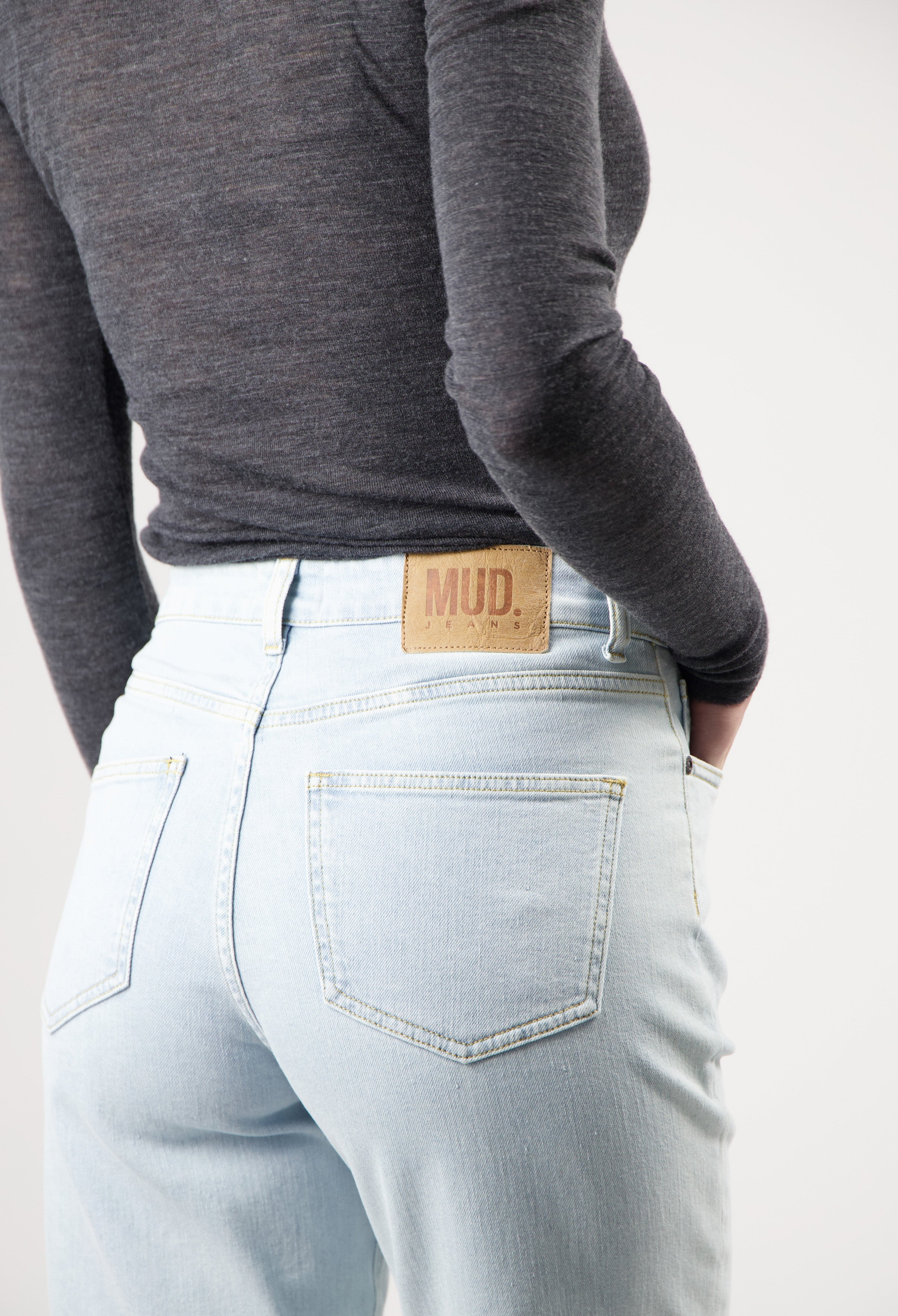 Light blue MUD Jeans made from organic cotton, featuring a high-waisted fit worn with a long-sleeve dark gray top.