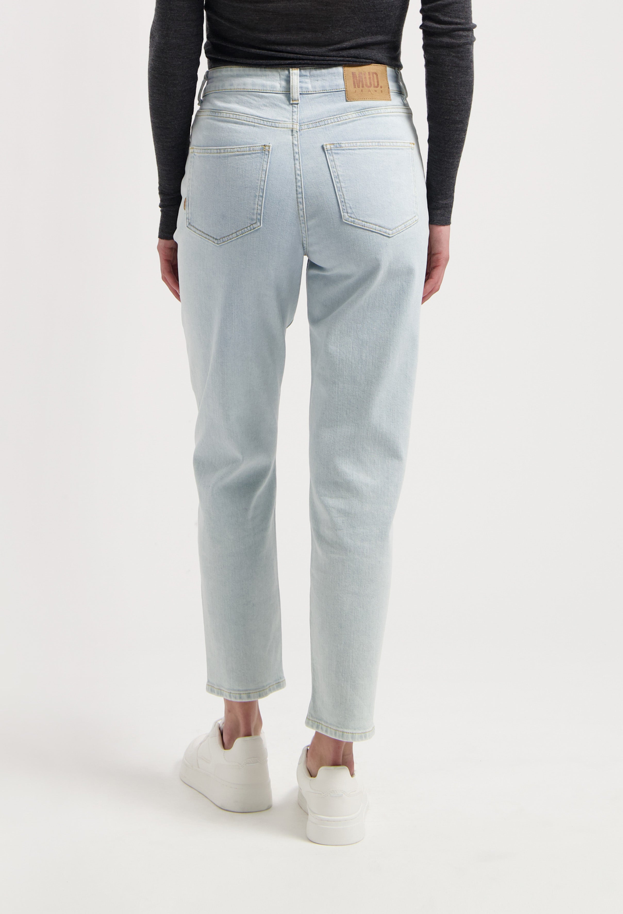 Light blue MUD Jeans made from organic cotton, showcasing high-waisted, straight-fit denim jeans worn with white sneakers.
