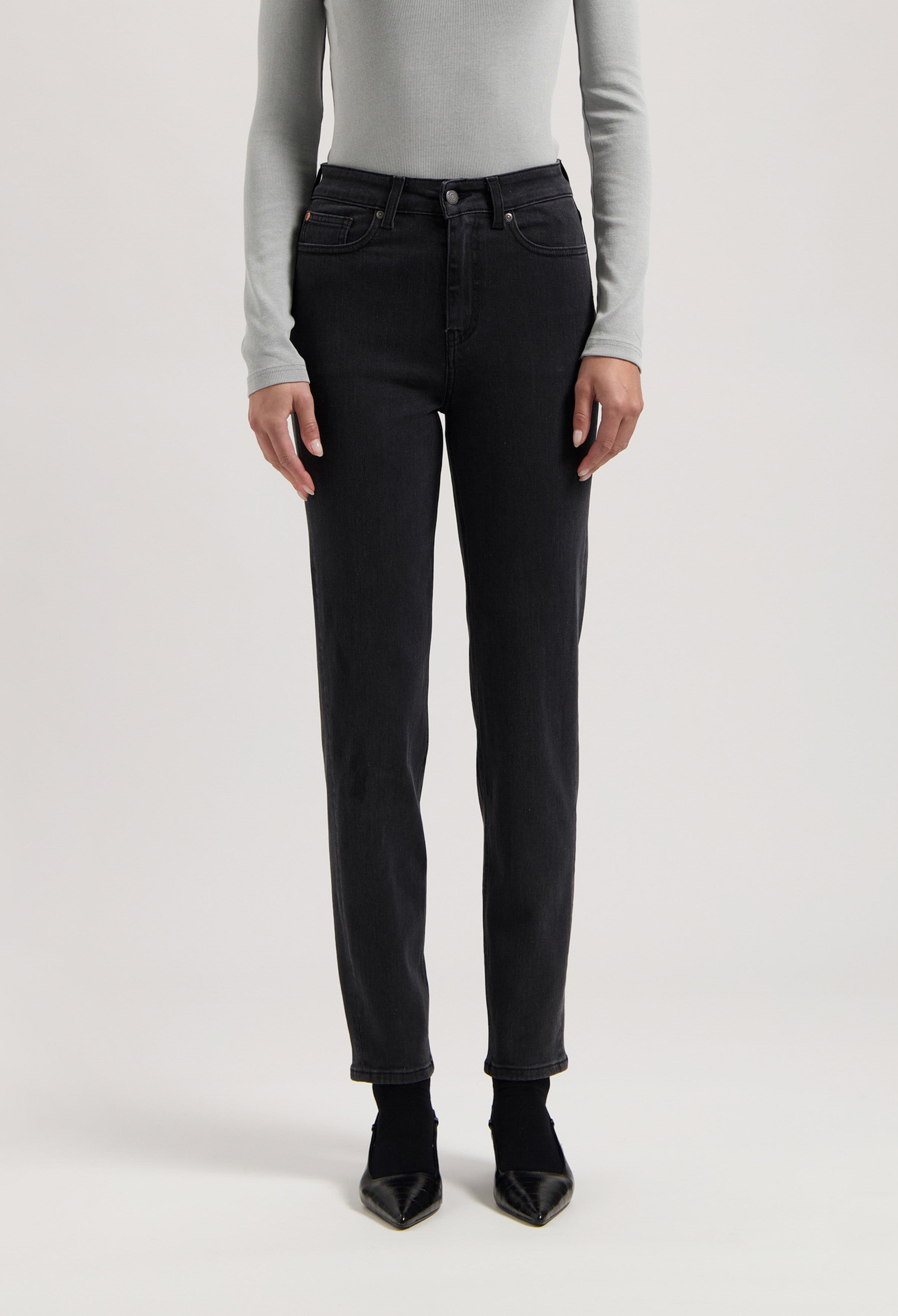 Person wearing black straight-leg jeans with a high-waist fit, paired with a light gray long-sleeve shirt and black heels.