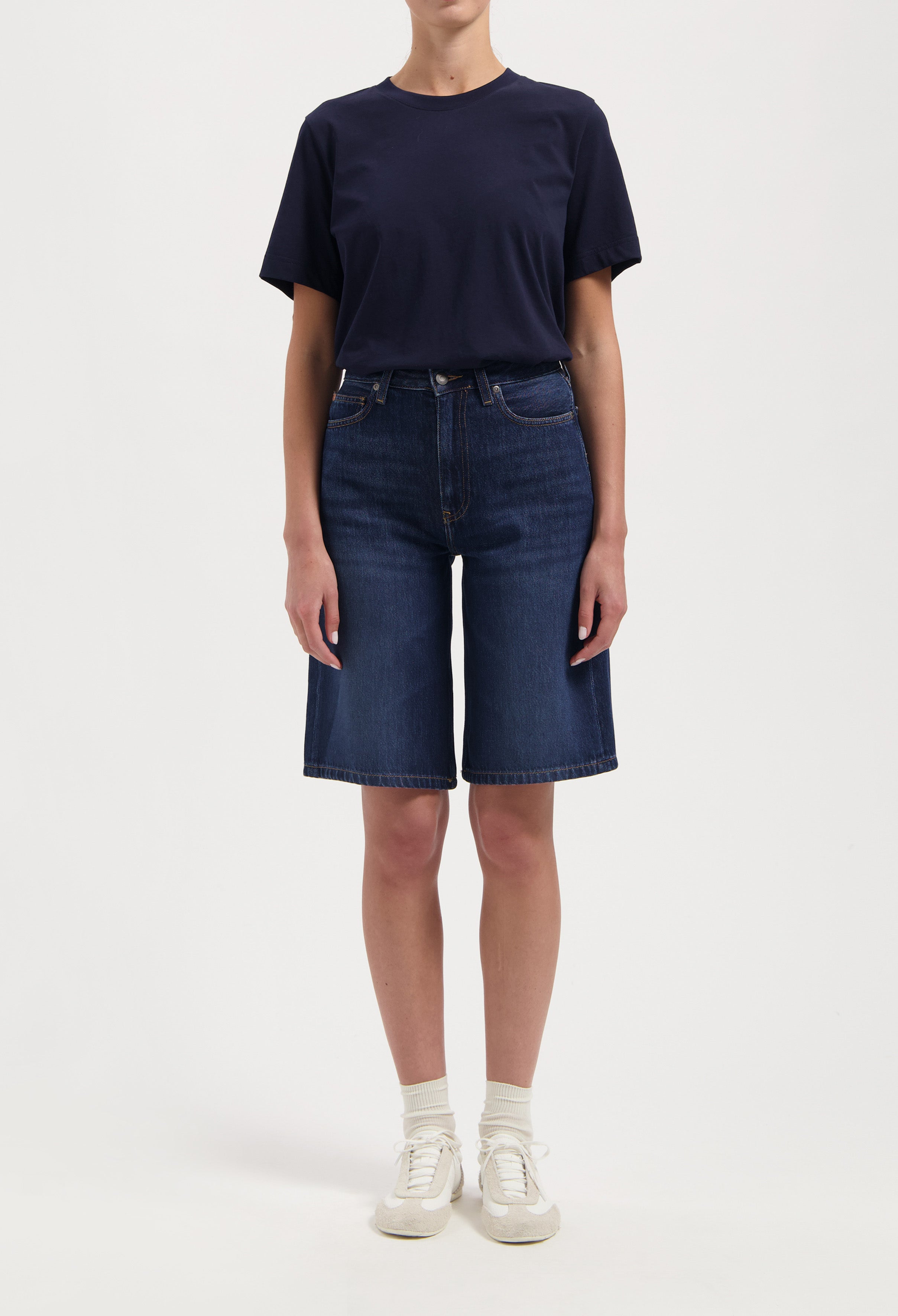 Casual outfit featuring a navy blue short-sleeve tee and knee-length dark denim shorts paired with white sneakers and socks.