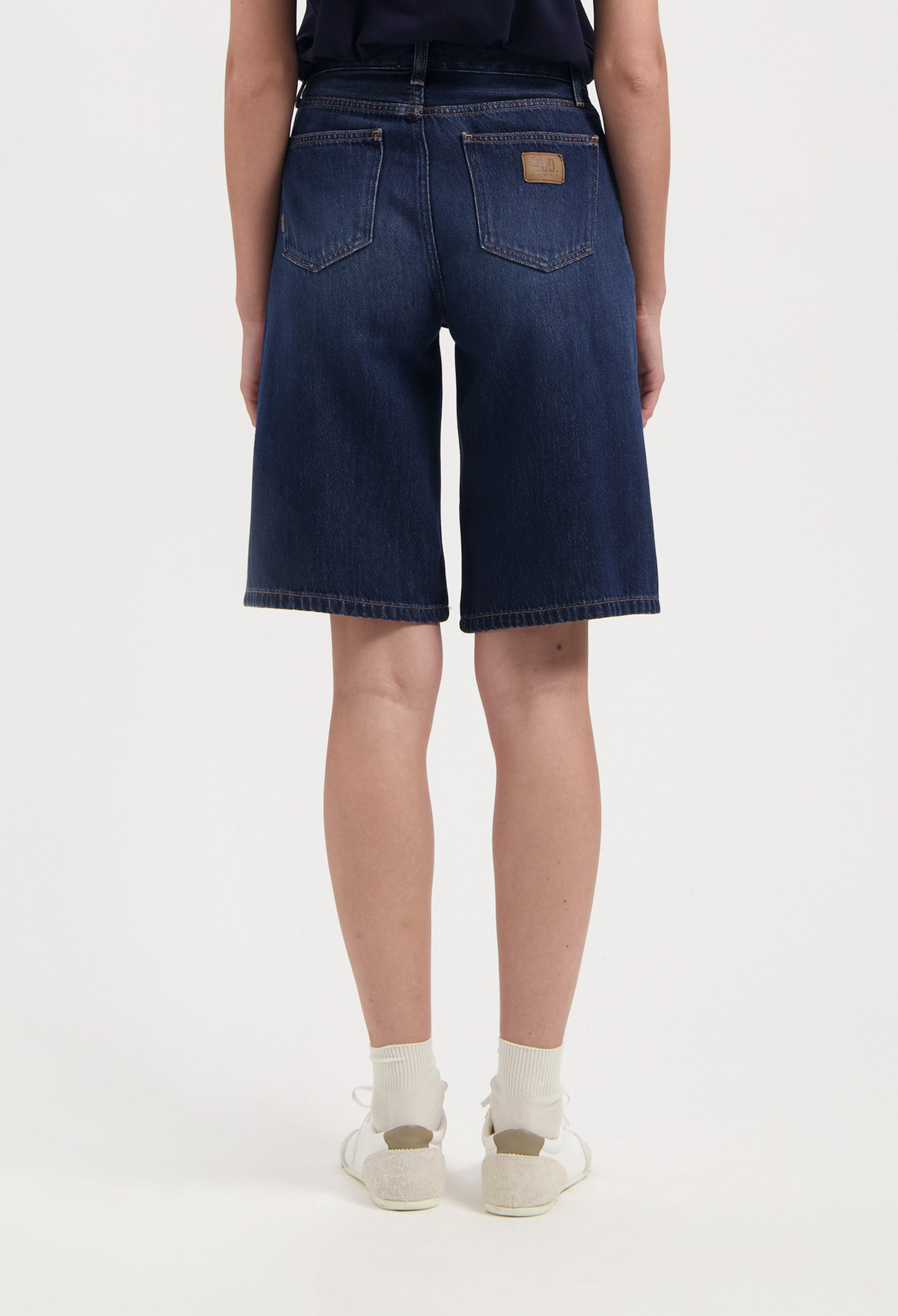 Back view of dark blue MUD Jeans denim shorts, showcasing high-waisted design with two pockets, paired with a navy top.