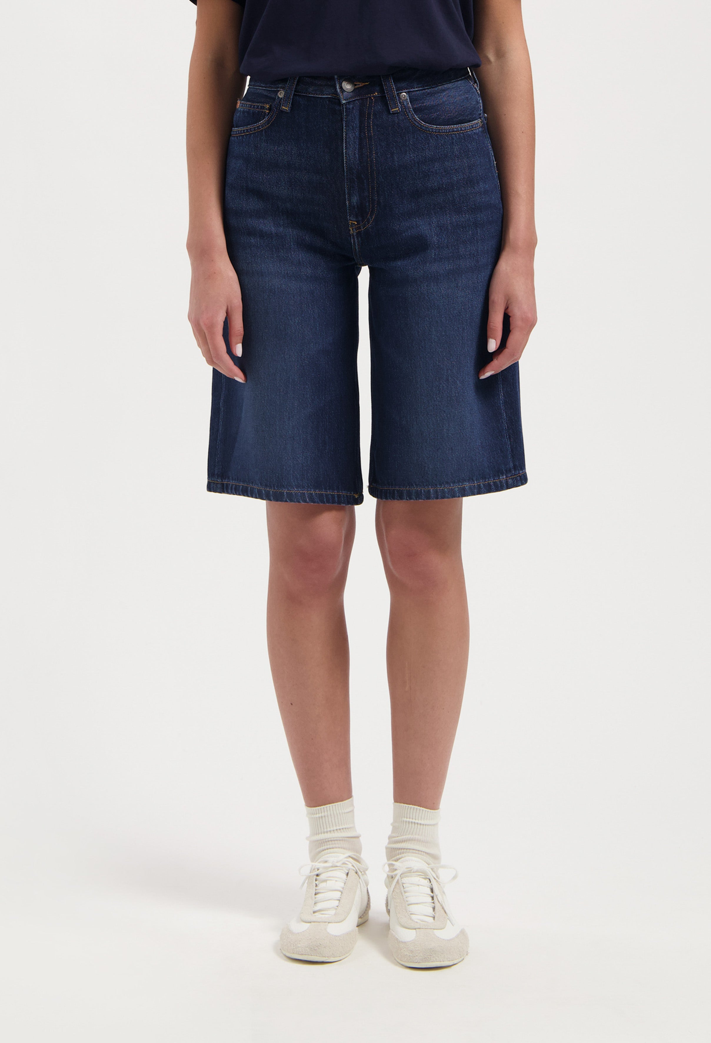 Dark blue denim knee-length shorts, showcasing a casual look with a black top and white sneakers for a relaxed style.