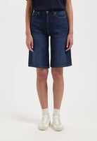 Dark blue denim knee-length shorts, showcasing a casual look with a black top and white sneakers for a relaxed style.