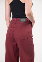 Organic cotton MUD Jeans in deep red, showcasing high-waisted fit with back pockets, paired with a black tank top.
