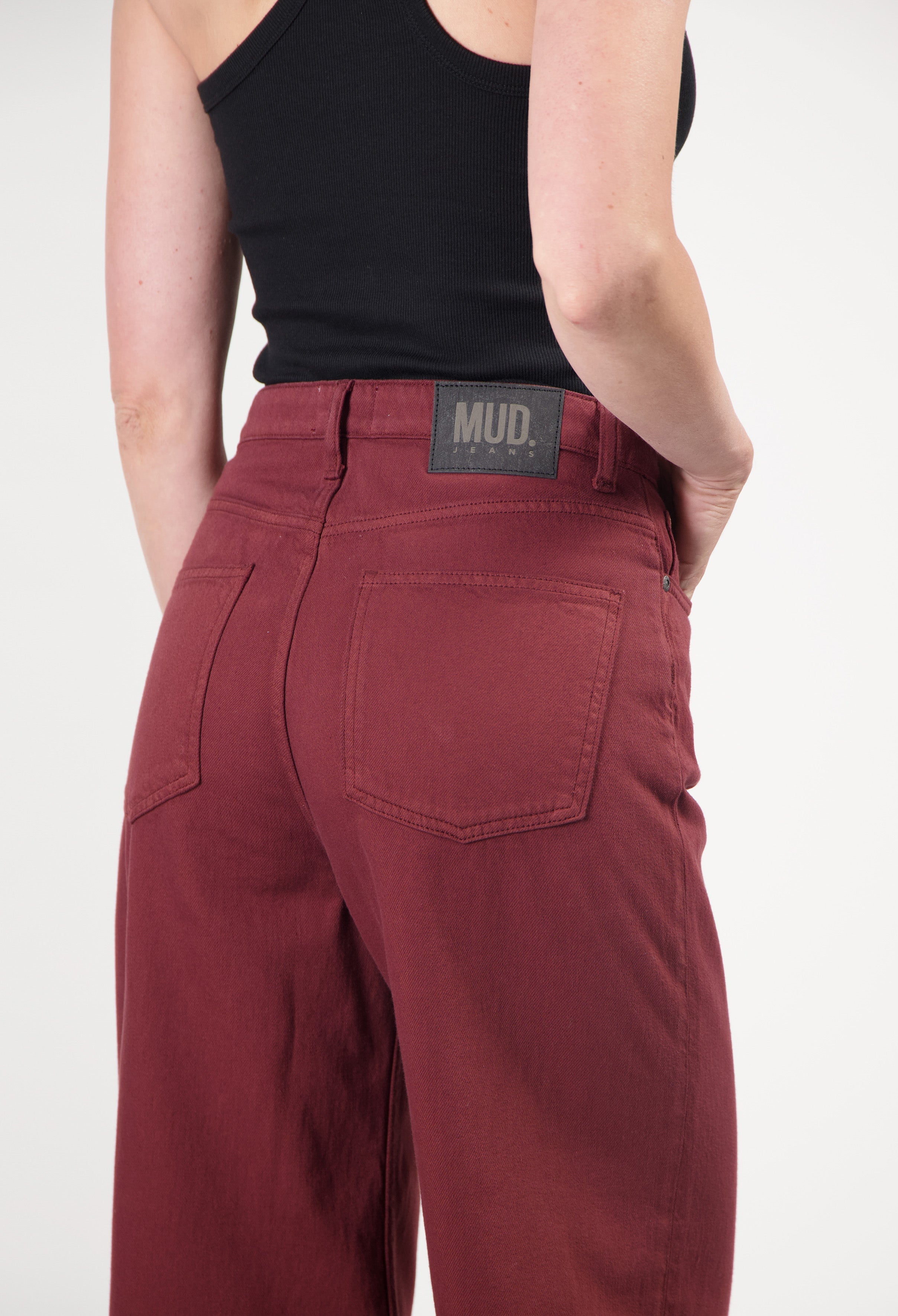 Organic cotton MUD Jeans in deep red, showcasing high-waisted fit with back pockets, paired with a black tank top.