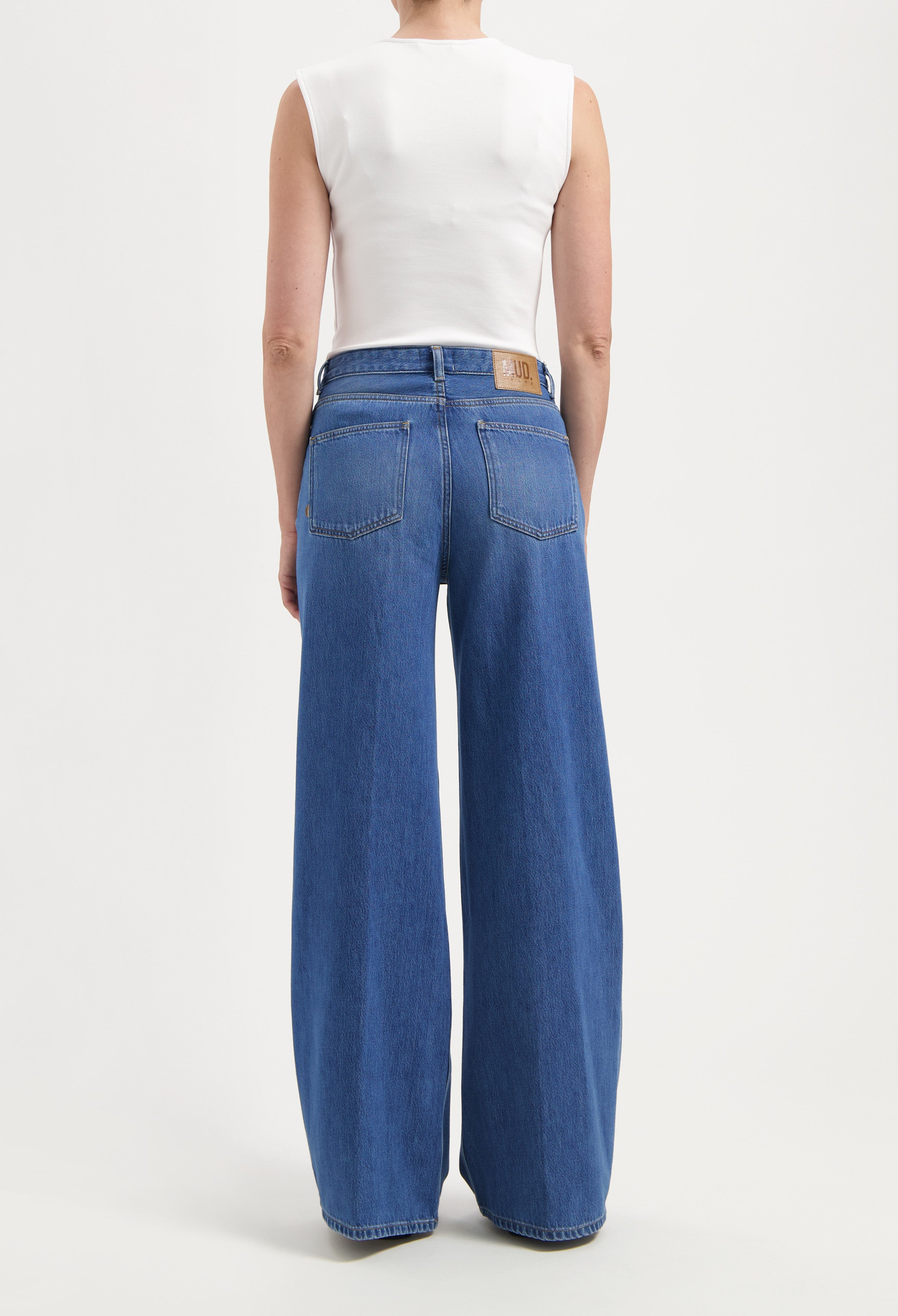 High-waisted wide-leg jeans in classic blue denim, worn with a sleeveless white top, showcasing casual style.