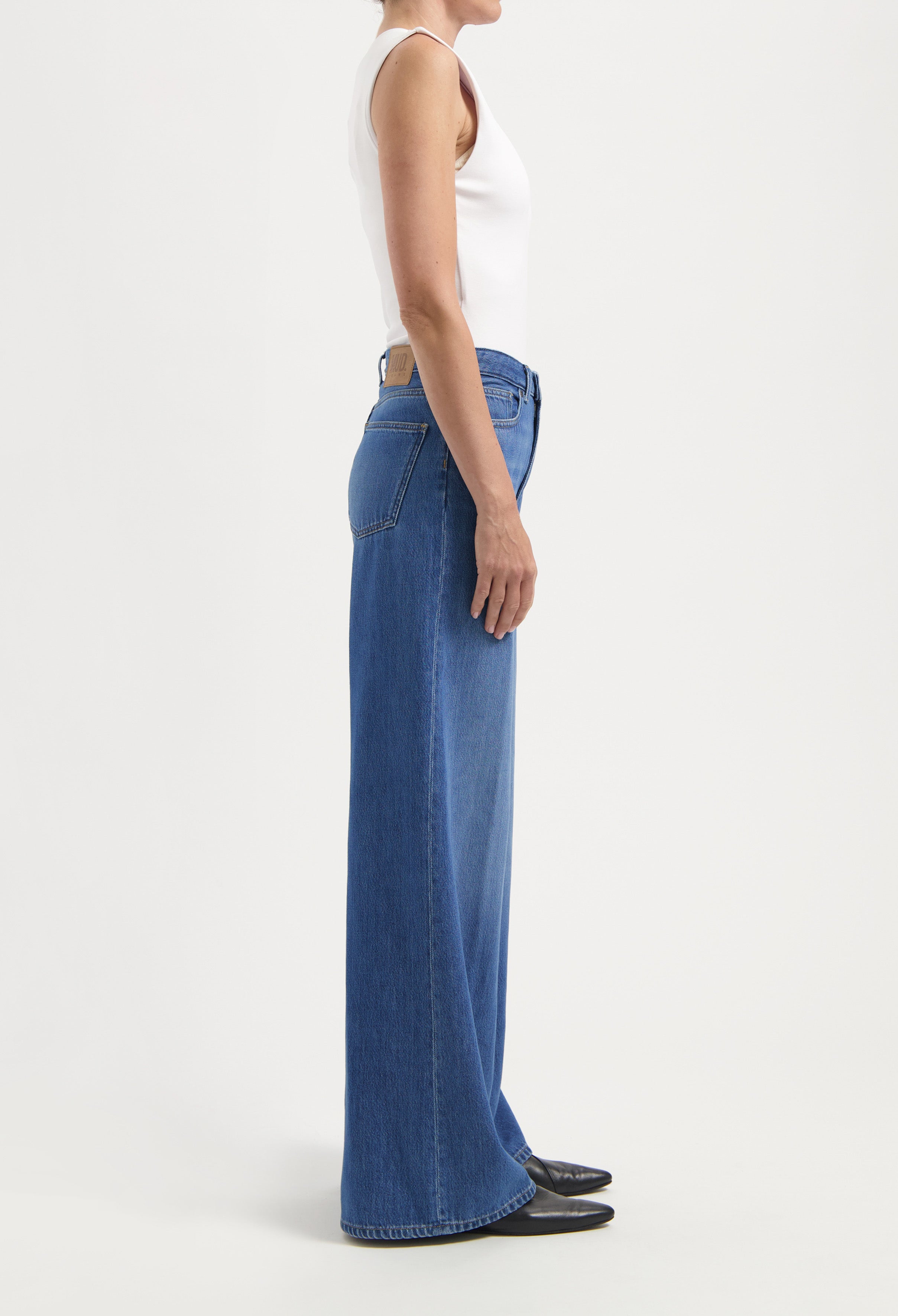 Wide-leg denim jeans in classic blue, high-waisted fit, styled with a sleeveless white top and black pointed shoes.