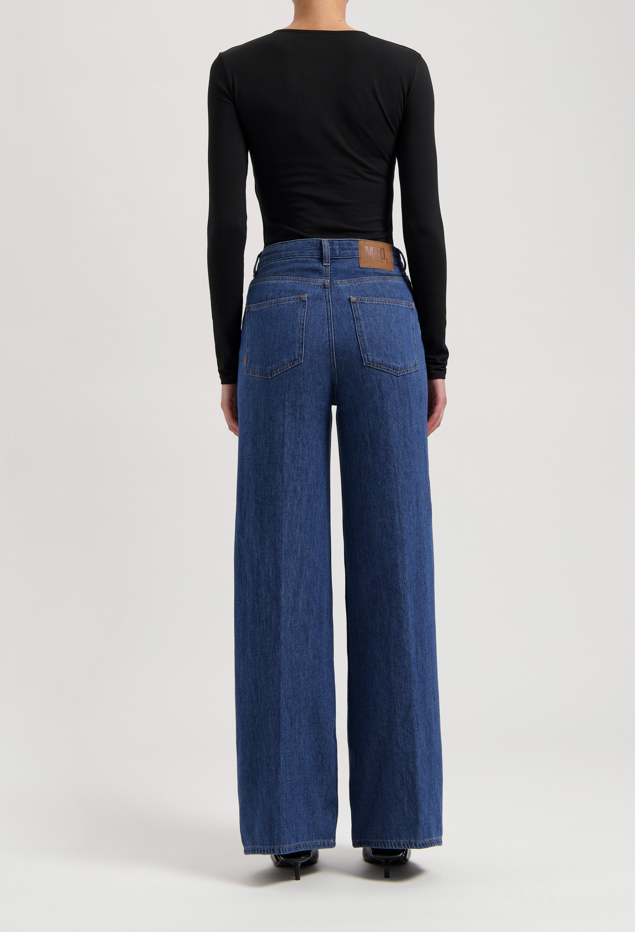 Wide-leg, eco-friendly blue jeans with a leather patch, paired with a sleek black long-sleeve top, showcasing sustainable fashion.