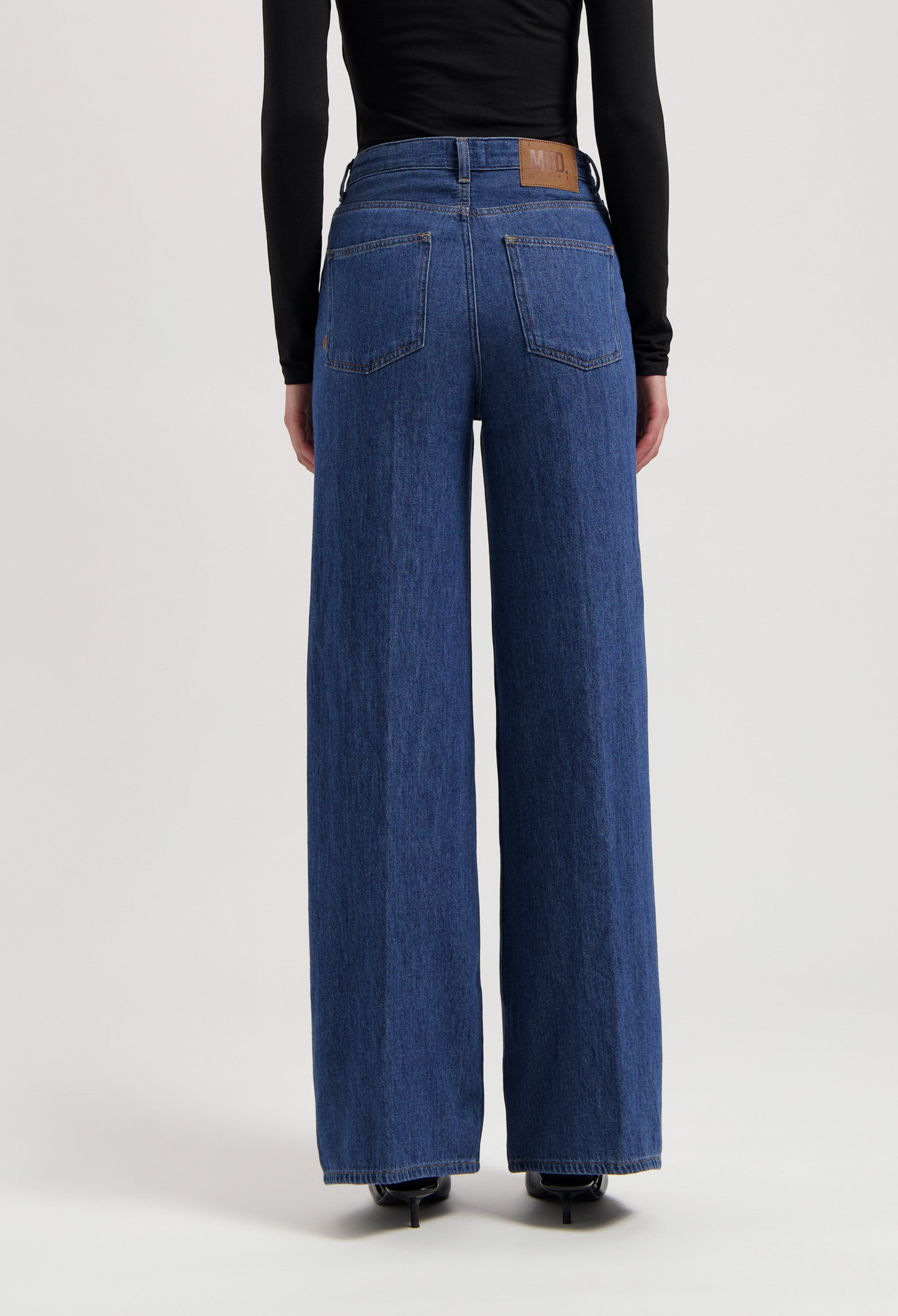 Wide-leg denim jeans in classic blue, featuring high-rise waist and rear pockets, paired with a sleek black long-sleeve top.