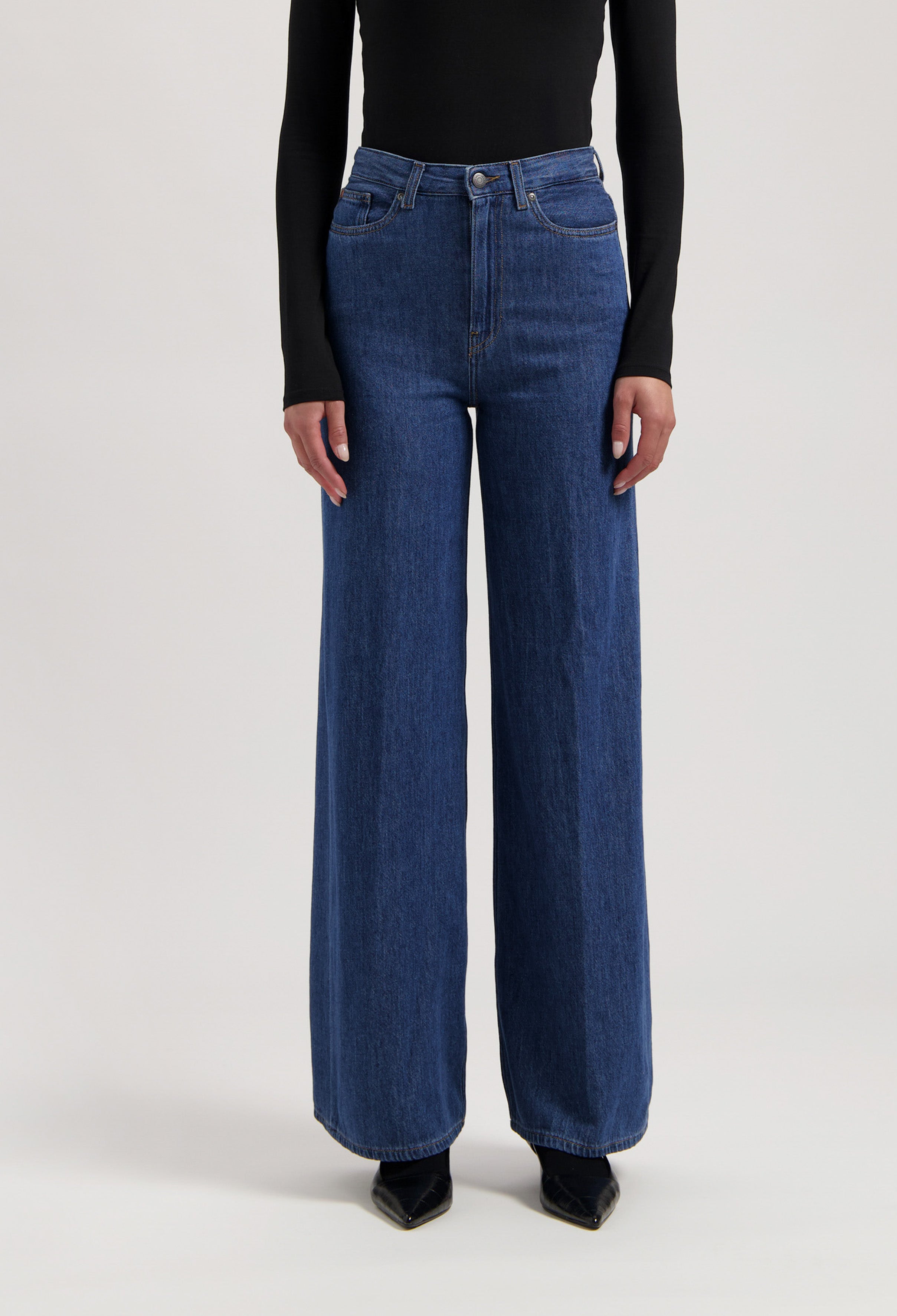 Wide-leg blue jeans in soft denim, paired with a black long-sleeve top; high-waisted with front button closure.