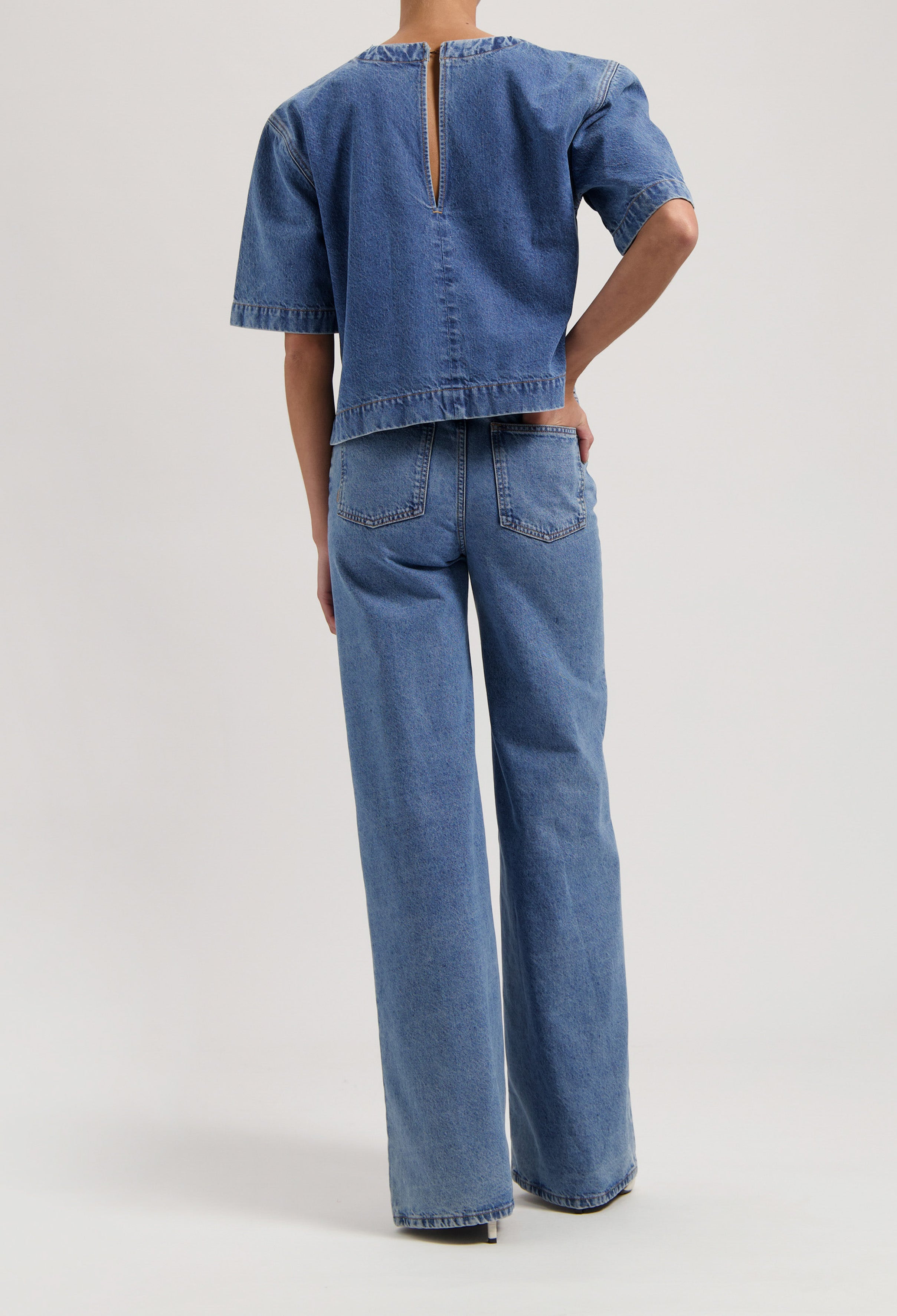 Back view of model wearing a matching light blue denim set with a short-sleeve top and wide-leg jeans.
