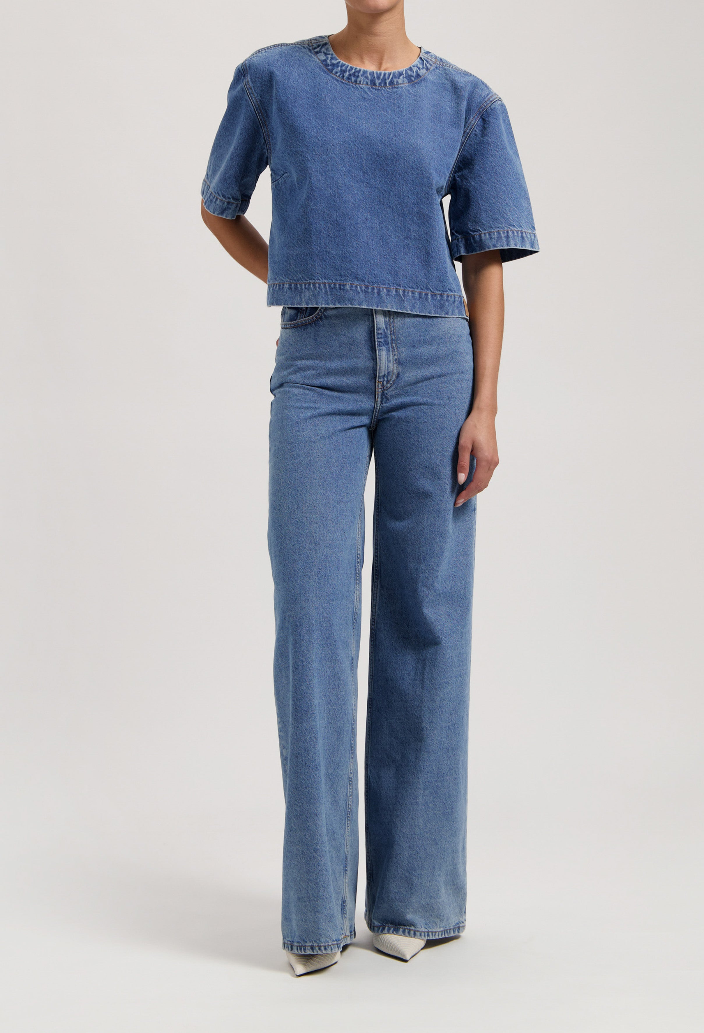 Model wearing blue denim two-piece outfit with short-sleeve top and wide-leg jeans, showcasing casual fashion style.