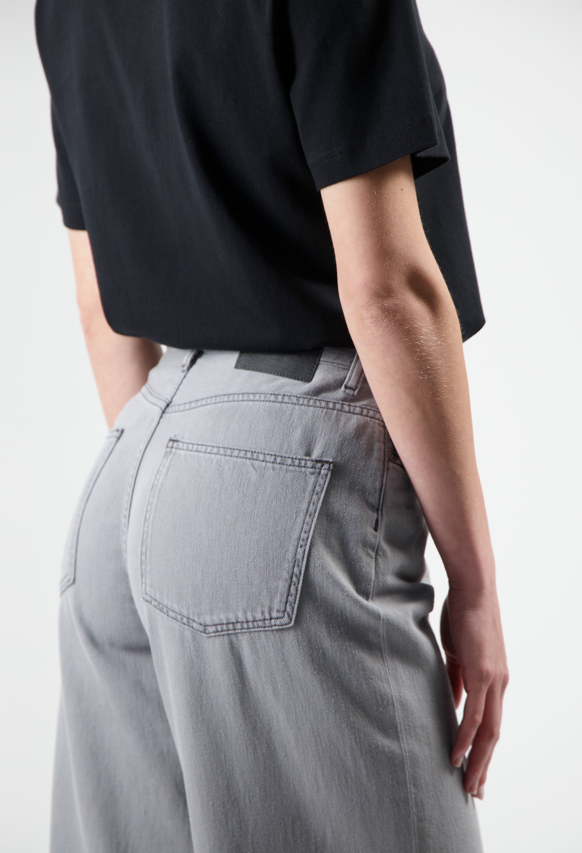 High-waisted gray cotton jeans with rear pockets, paired with a black short-sleeve top, showcasing modern casual style.