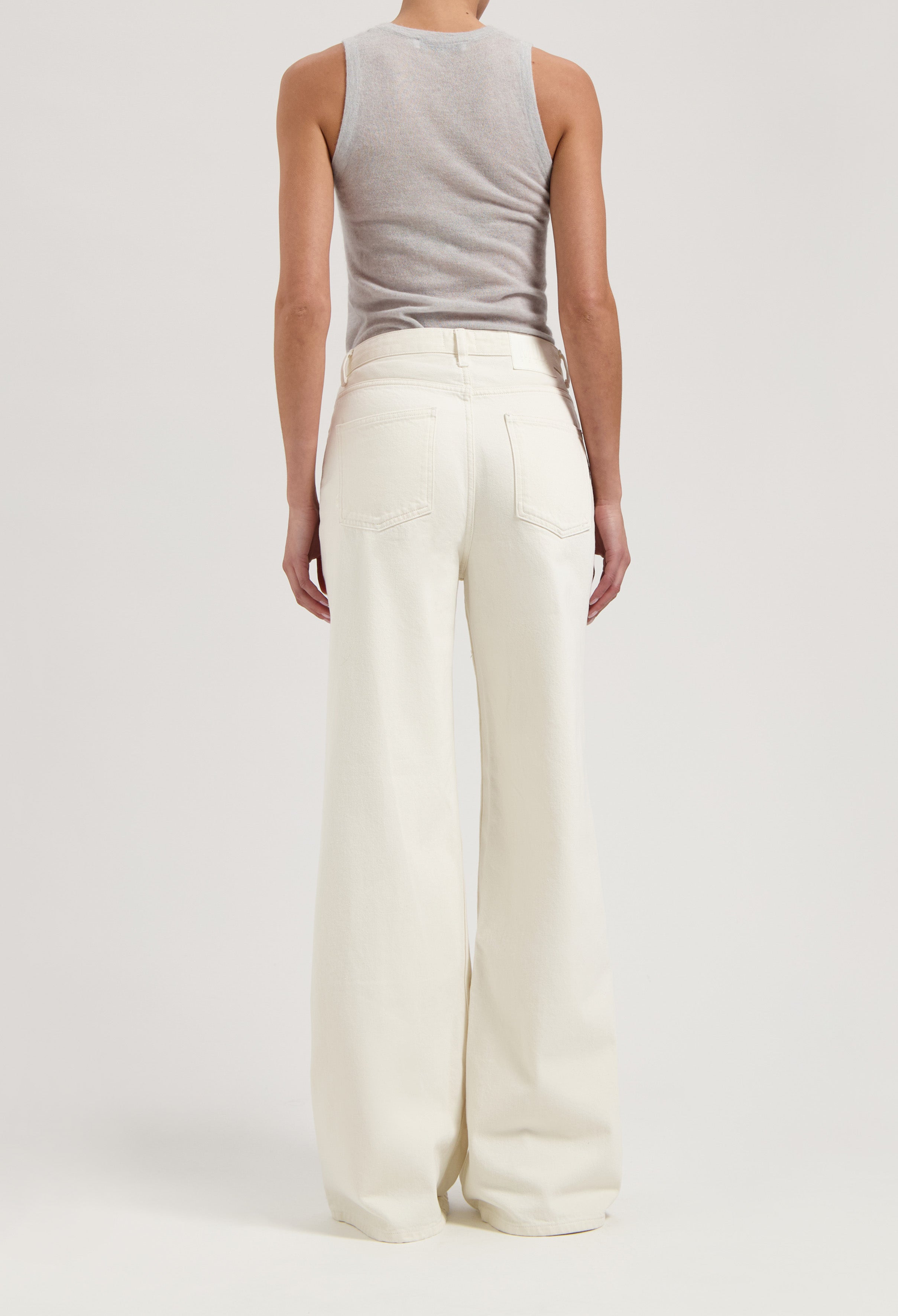 Back view of flared white denim pants worn with a light gray sleeveless top, showcasing modern and stylish casualwear.