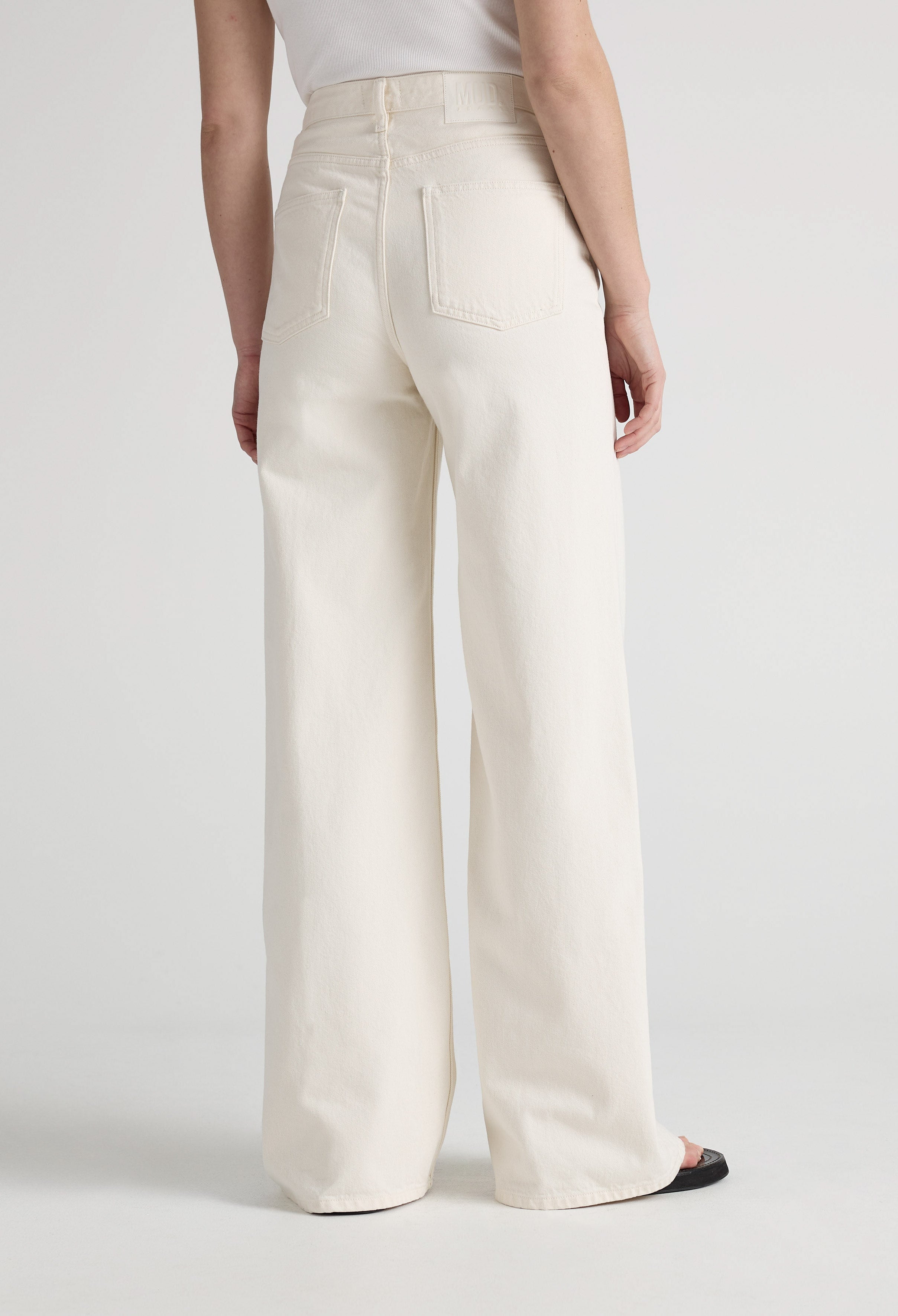 Wide-leg cream denim jeans from MUD Jeans, showing back pockets and high waist, paired with black shoes.