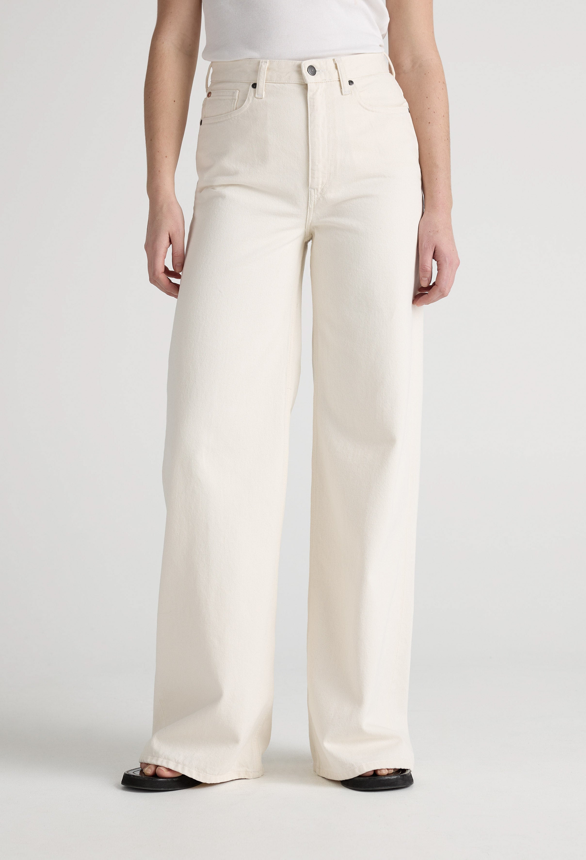 Wide-leg cream jeans in organic cotton, displaying high-waisted design paired with a simple white tank top.