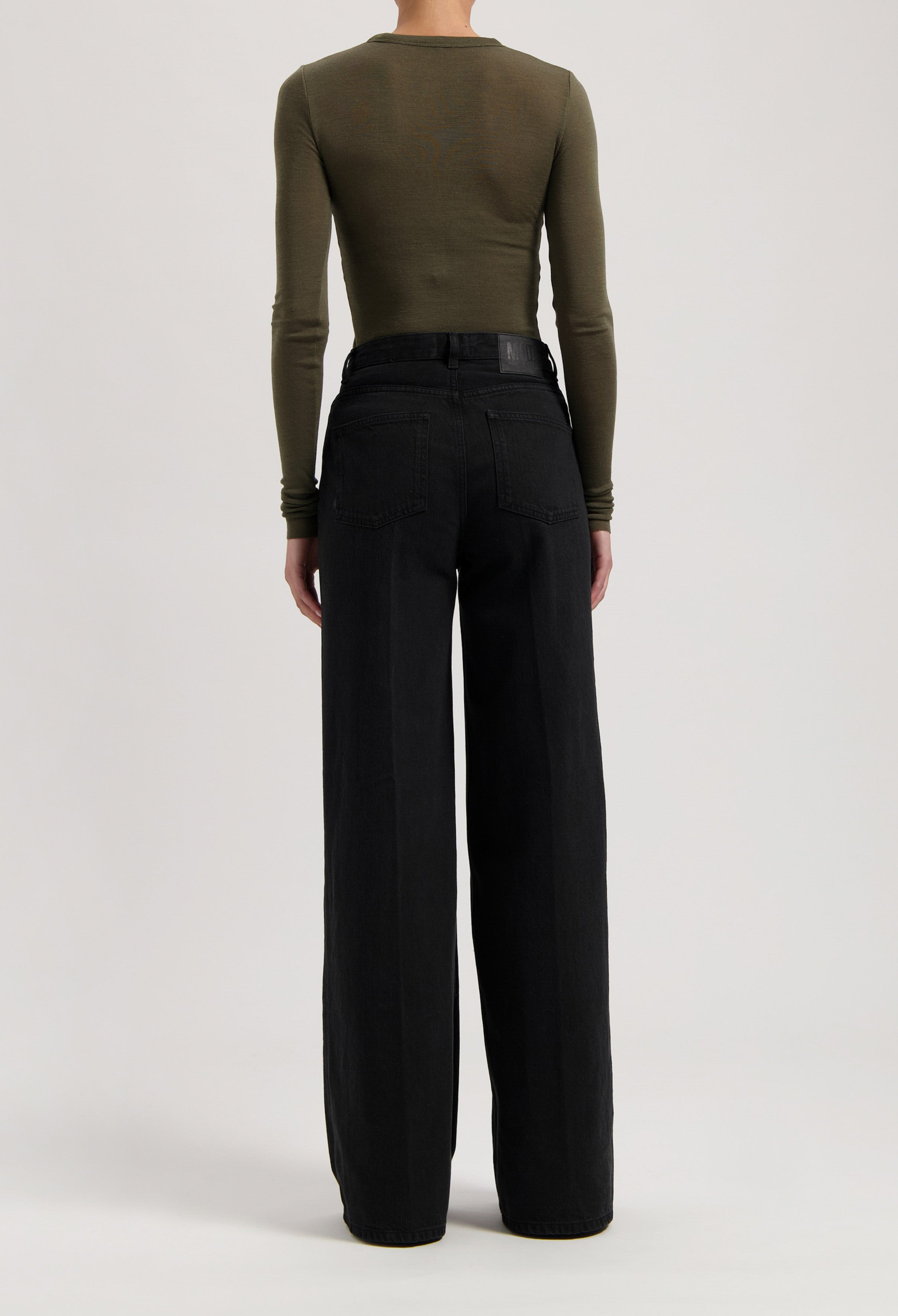 Rear view of a model wearing high-waisted black wide-leg jeans paired with an olive green long-sleeve top.
