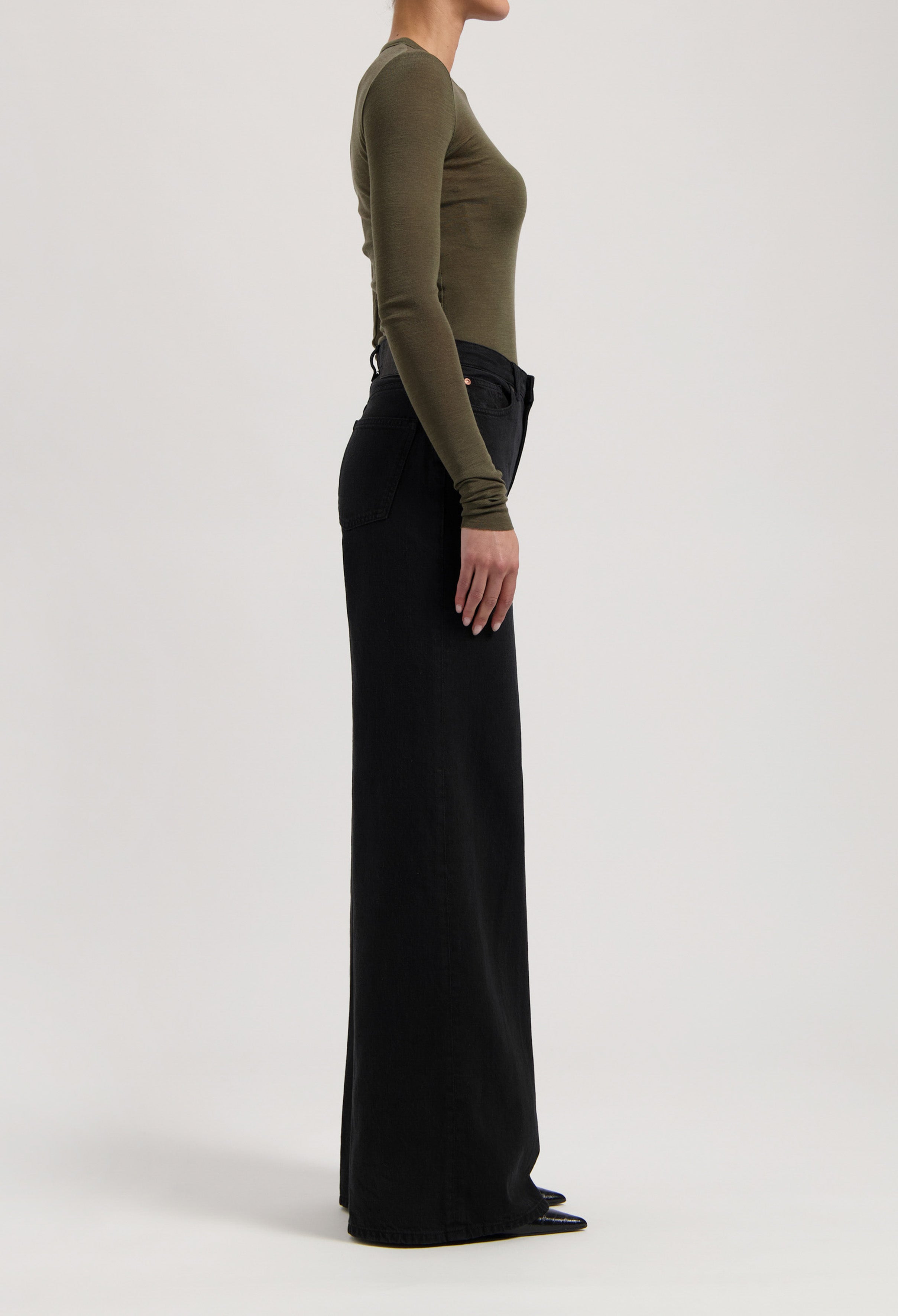 Side view of a model wearing high-waisted black wide-leg pants paired with an olive green long-sleeve fitted top.