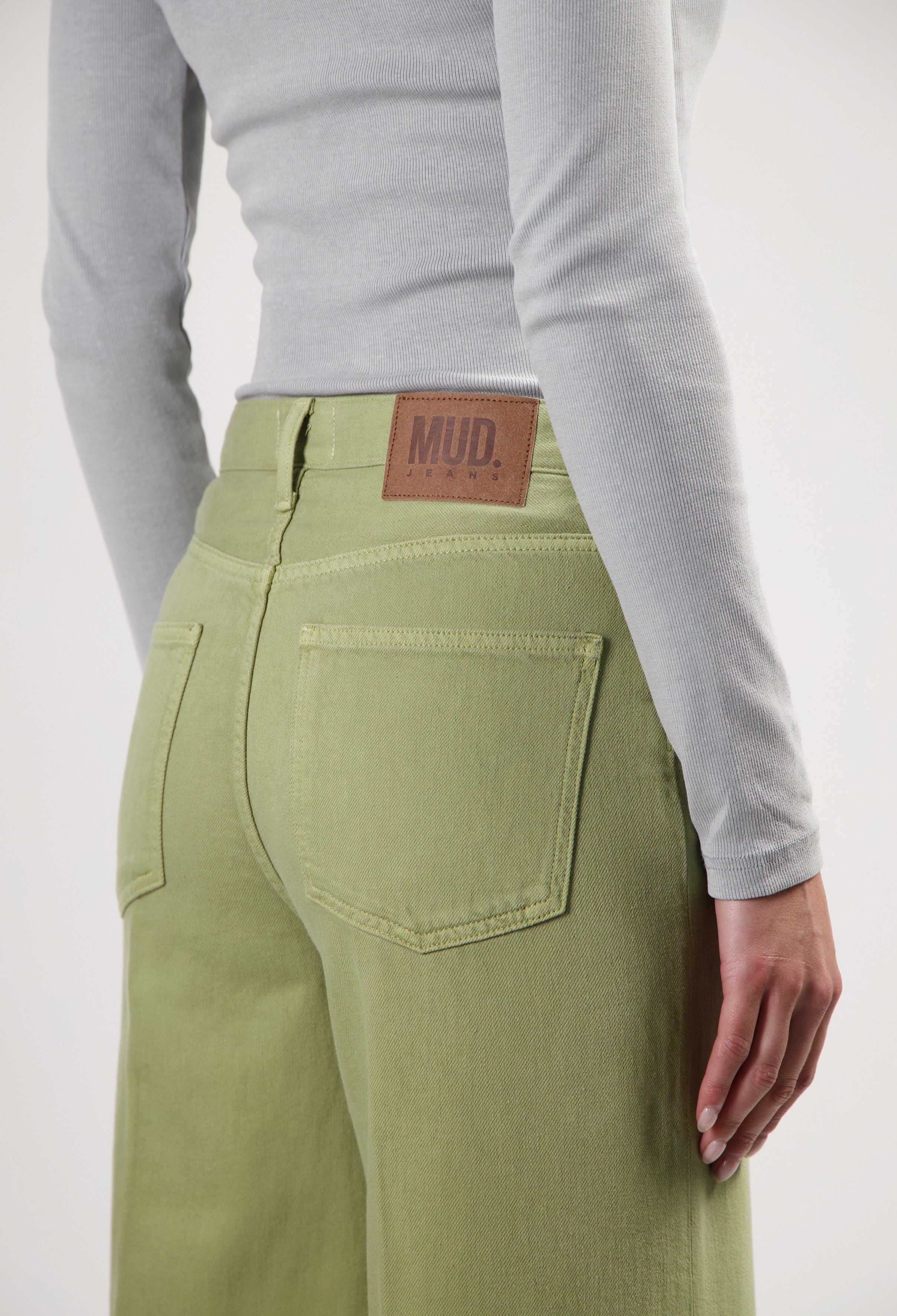 Light green sustainable MUD Jeans crafted from organic cotton, featuring high-waisted design worn with a gray ribbed top.