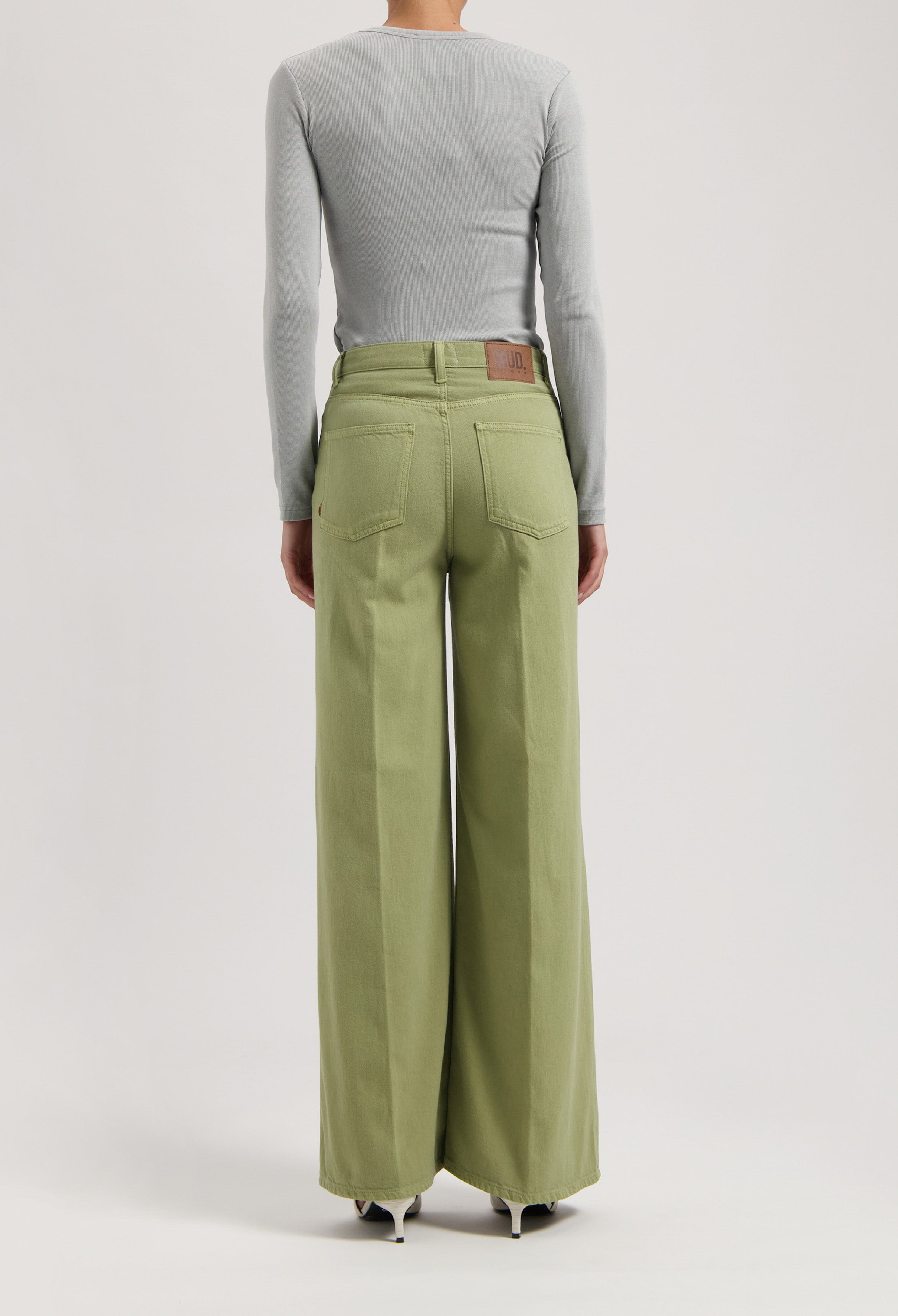 High-waisted, wide-leg MUD Jeans in light green organic cotton worn with a fitted gray long-sleeve top.