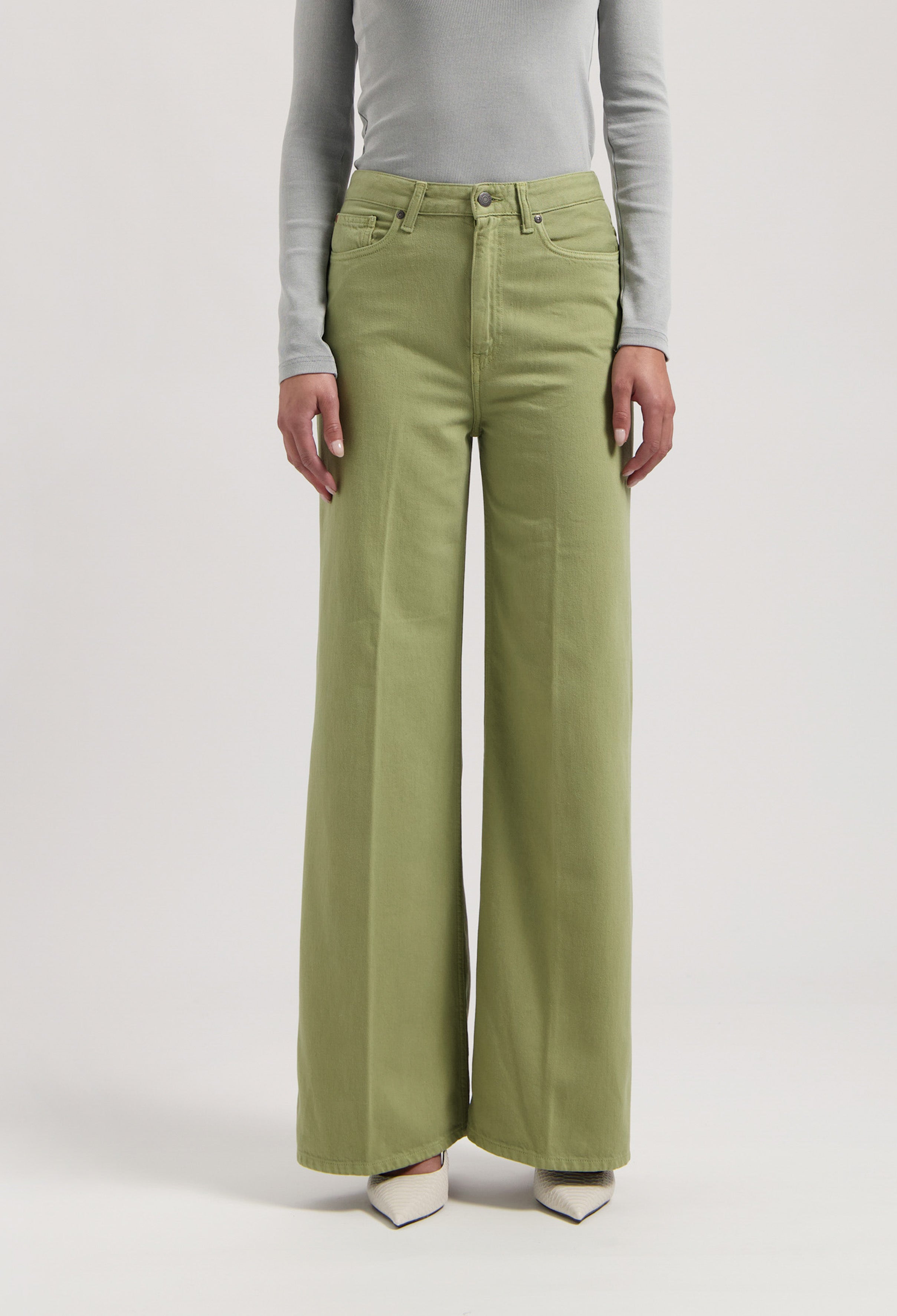 Green wide-leg jeans made from cotton, worn with a light gray long-sleeve top, showcasing a stylish casual look.