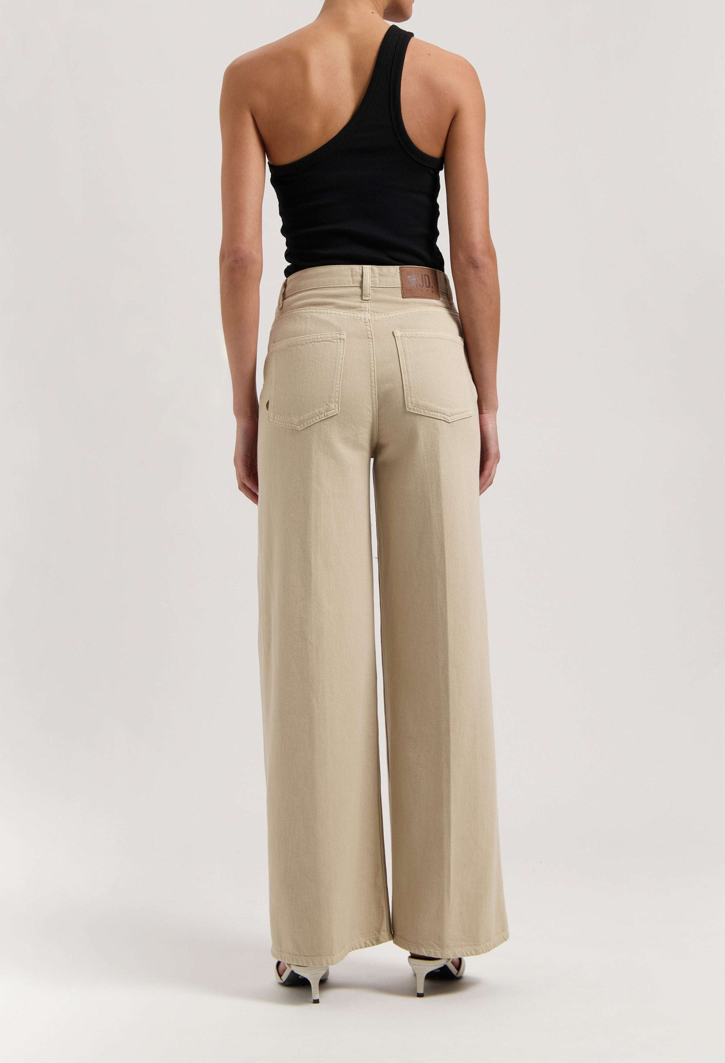 Wide-leg beige trousers in a minimalist design, paired with a black asymmetrical sleeveless top, showcasing modern casualwear.