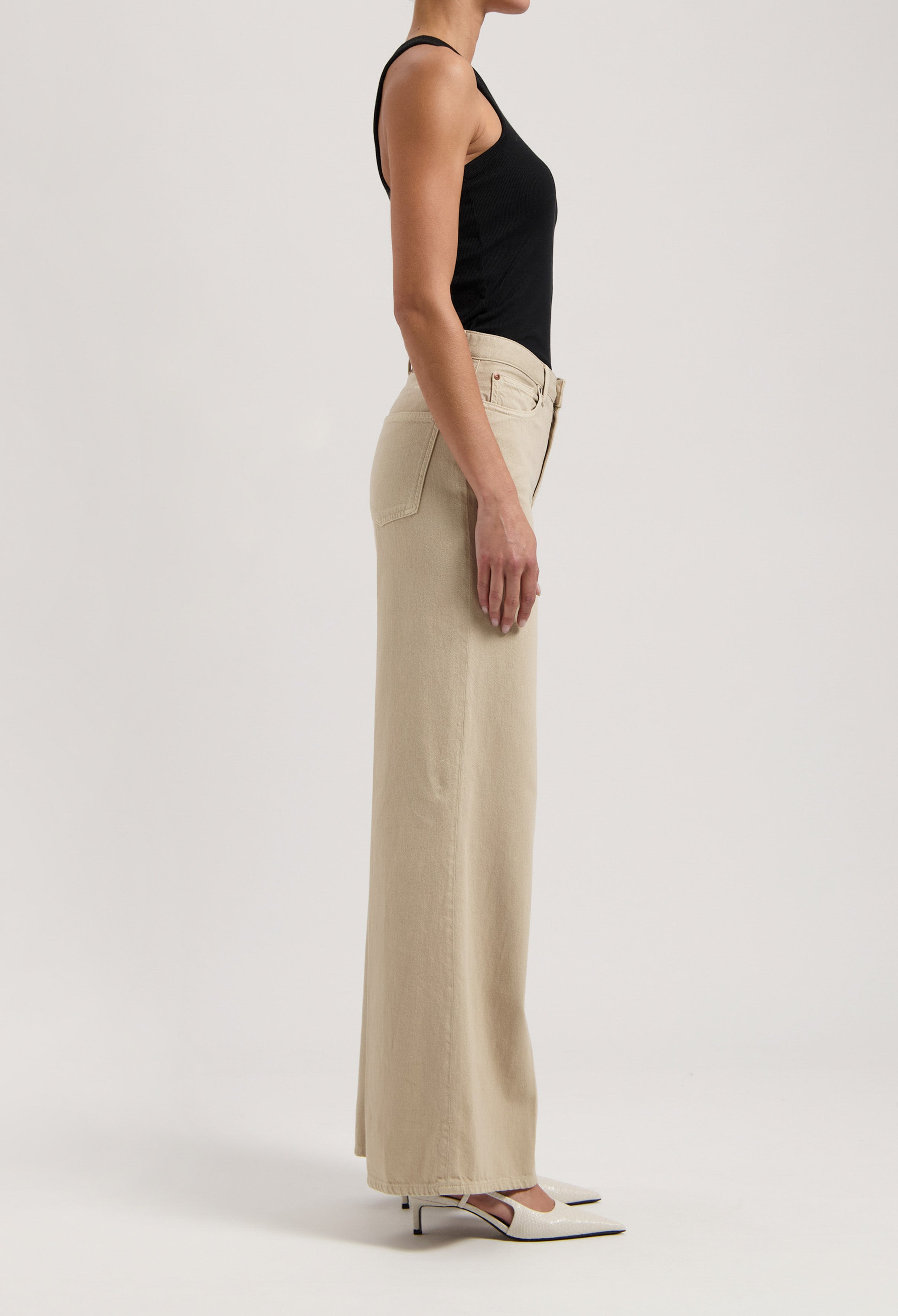 A woman wearing a black tank top and beige wide-leg pants, highlighting a side profile of minimalist fashion style.