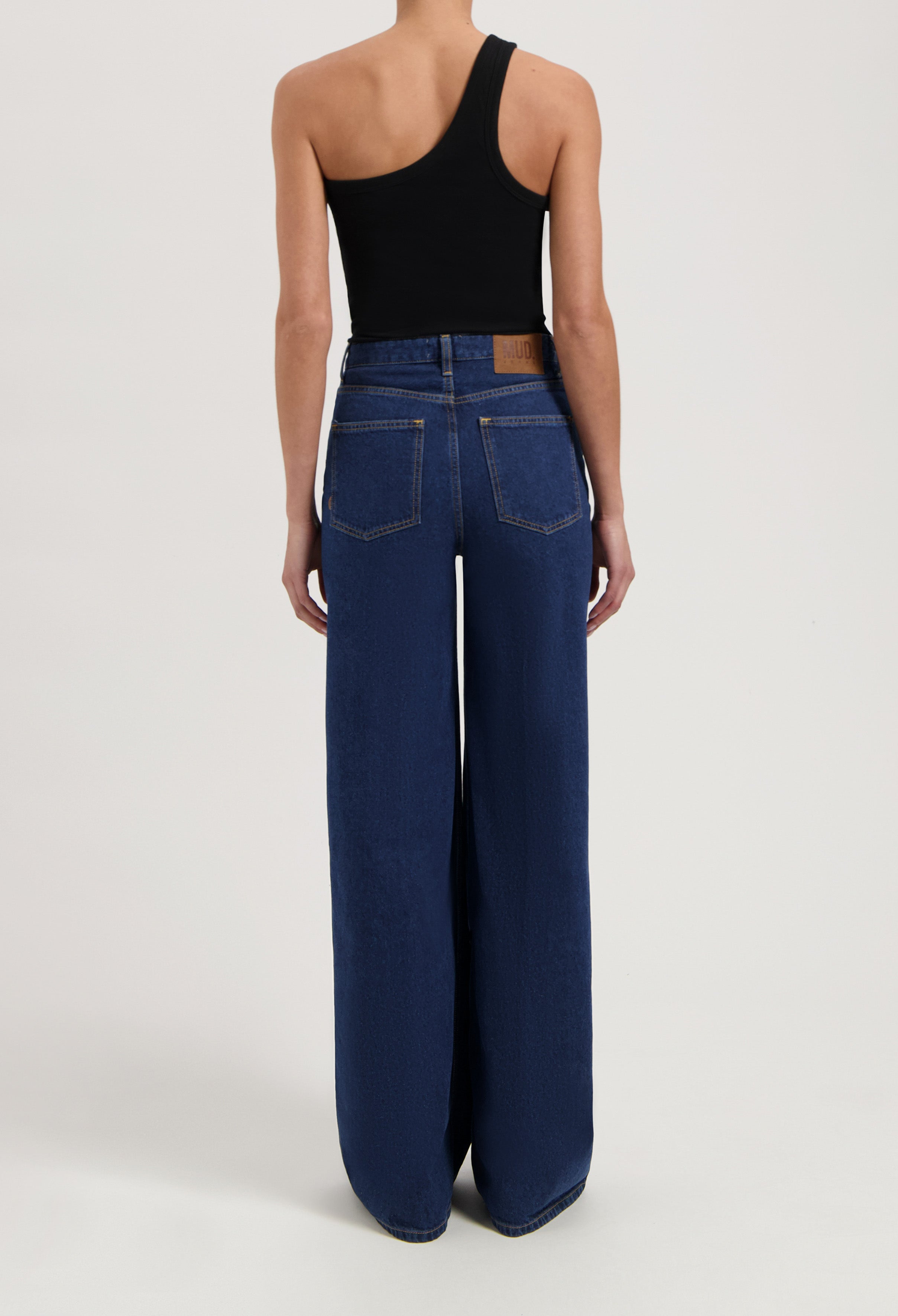 Wide-leg blue denim jeans from MUD Jeans, made from organic cotton, shown worn with a sleeveless black top.